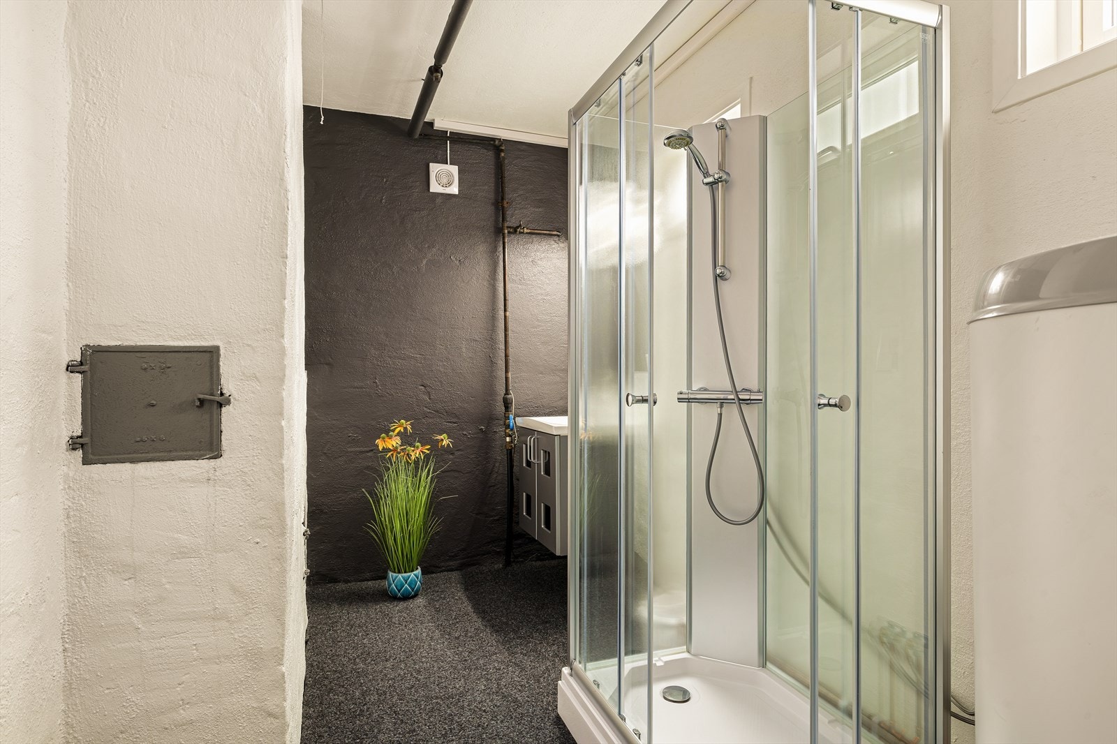 Bad i 1.etasje med adkomst fra hall. Rommet er utstyrt med vaskeservant i innredning og lukket dusjkabinett. En varmtvannsbereder på 250 liter er plassert i rommet. Ventilasjon skjer via mekanisk ventilasjon og lufteventil på vegg. Galleribilde