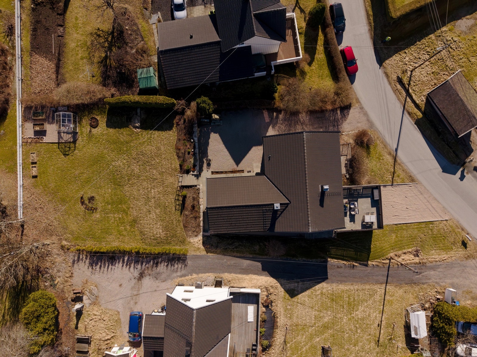 Oversiktsbilde som viser tomten i bakkant. Stor, delvis skrånede gressplen. Drivhus og dyrkekasser - trapp og steingjerde mellom hage og gårdsplass. Galleribilde