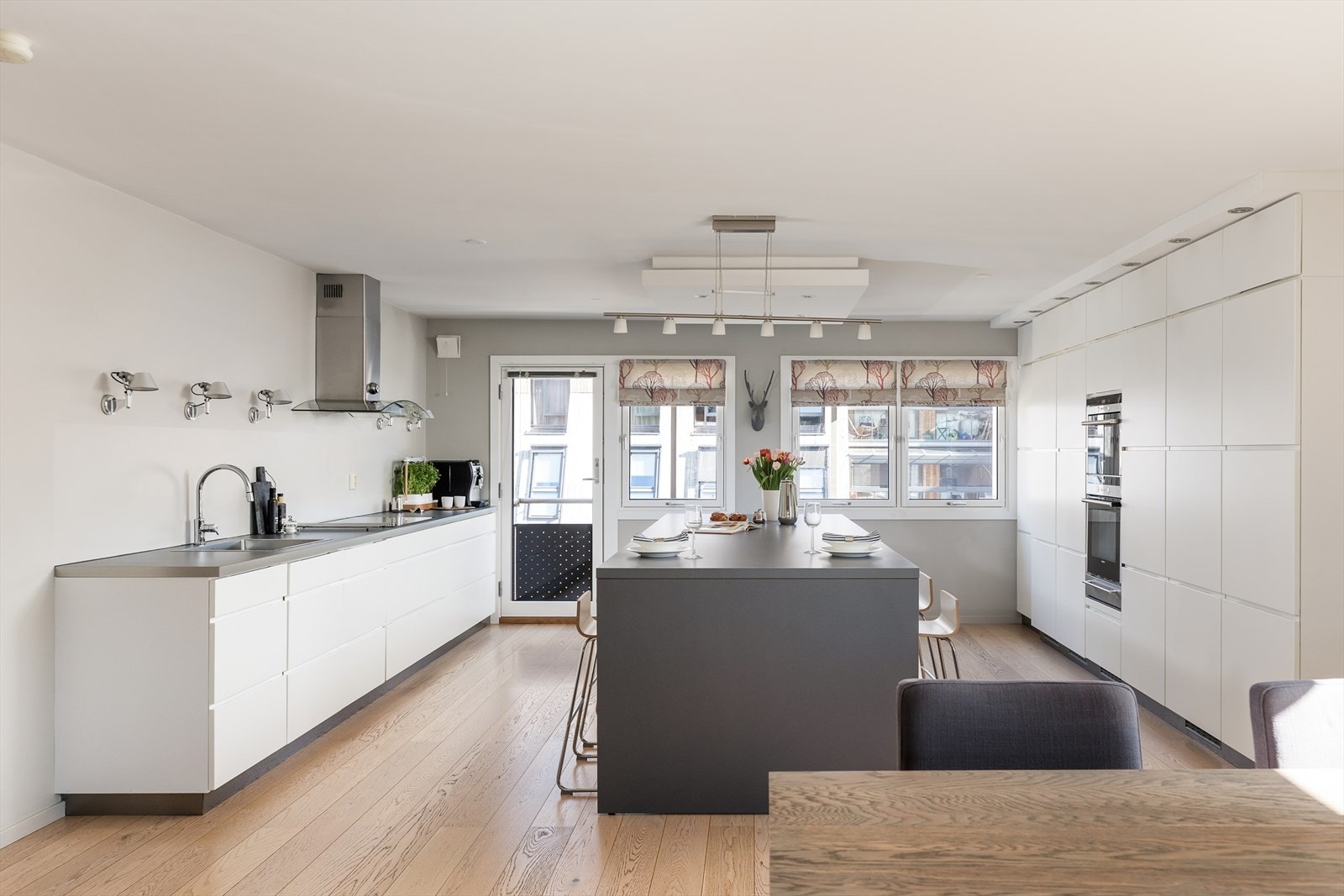 Moderne kjøkken fra 2013 med glatte, hvite fronter og en stor kjøkkenøy som blir et naturlig samlingspunkt. Galleribilde