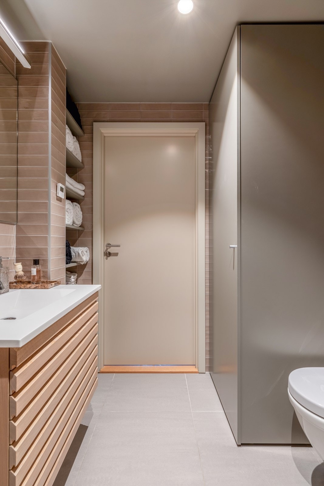 Rommet er helfliset og har et tidløst uttrykk som kombinerer funksjonalitet med estetikk. Vannbåren gulvvarme sørger for en behagelig og lun atmosfære, og understreker badets helhetlige kvalitetsfølelse. Galleribilde