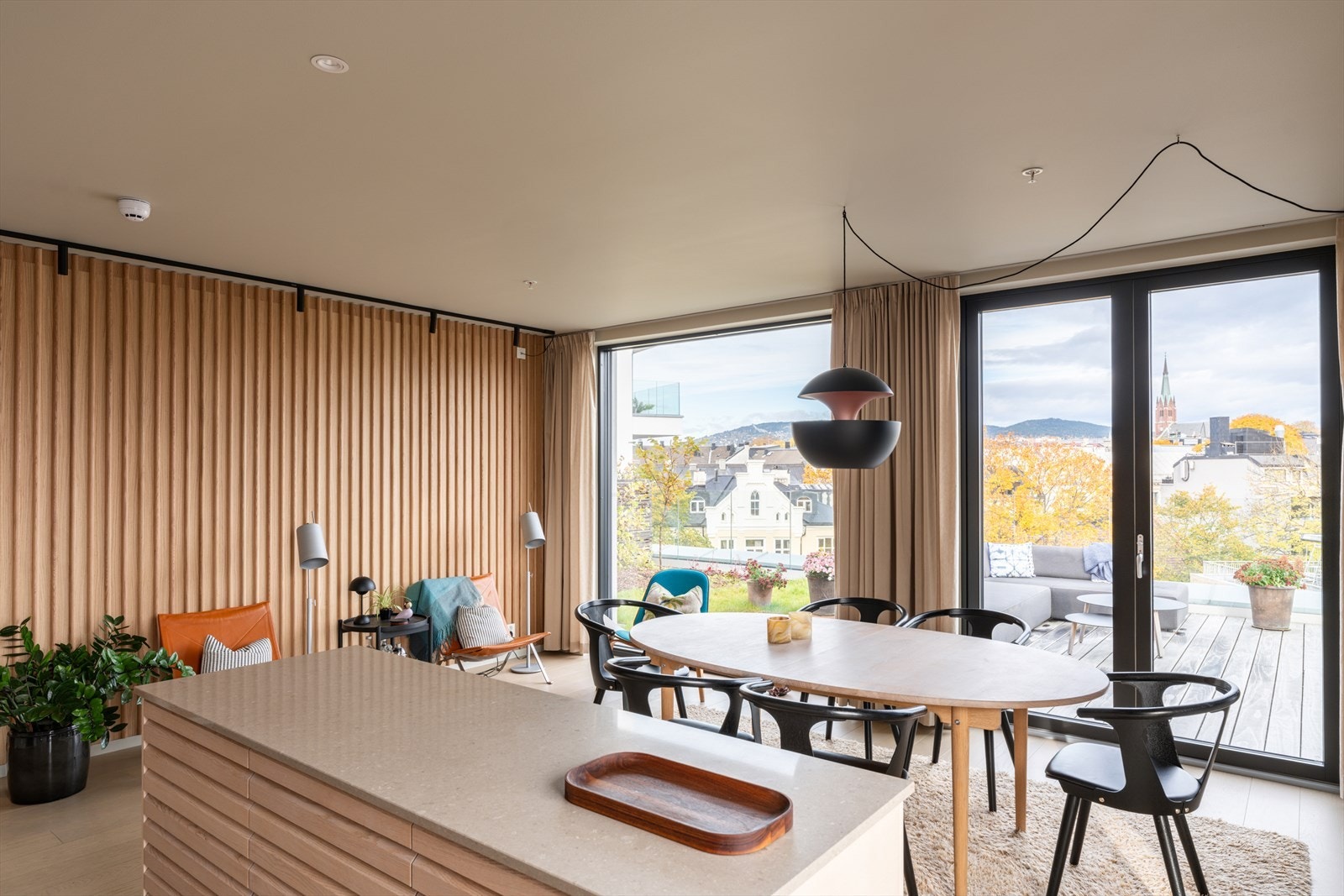 En elegant spilevegg i tre gir rommet karakter og varme, mens store vinduer slipper inn rikelig med dagslys. Galleribilde