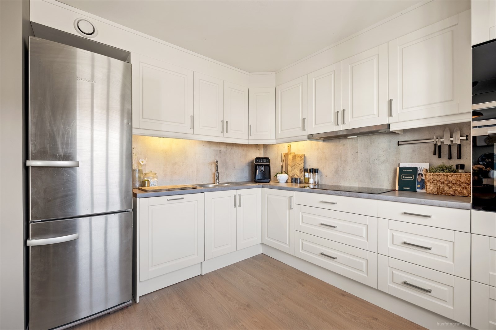 Klassisk og delikat kjøkkeninnredning med hvite profilerte fronter og benkeplate av laminat. Galleribilde