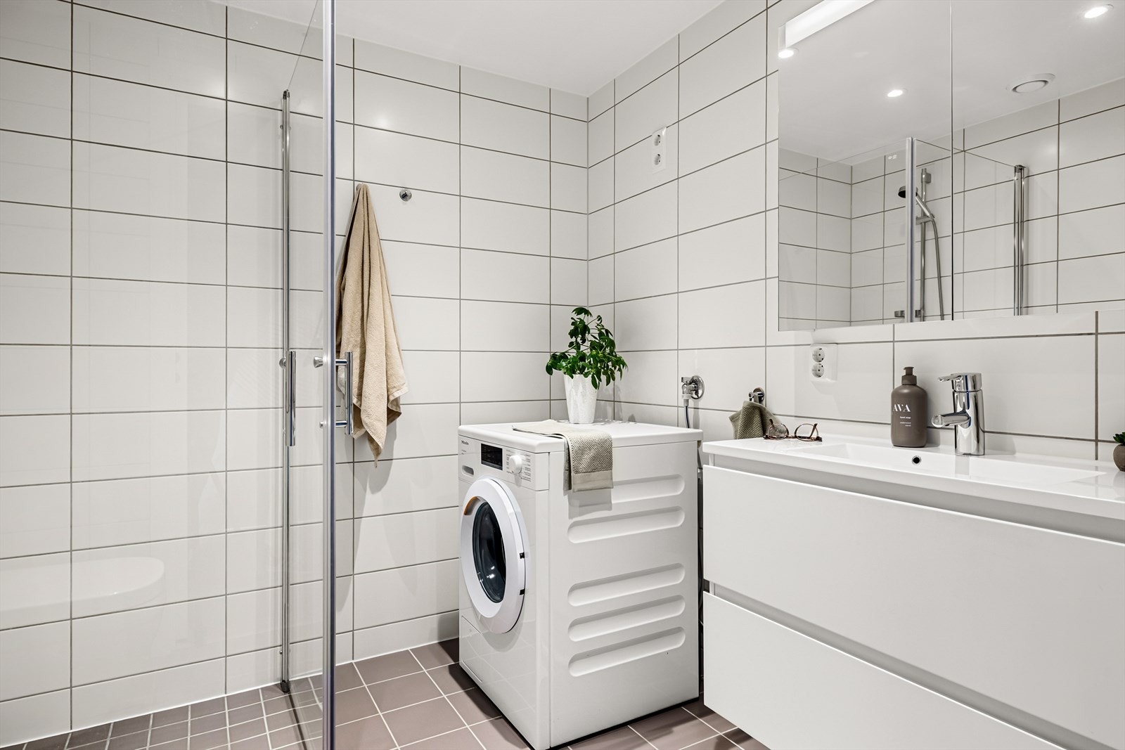 Det er utstyrt med dusj med glassvegger, vegghengt toalett, baderomsinnredning og opplegg for vaskemaskin Galleribilde