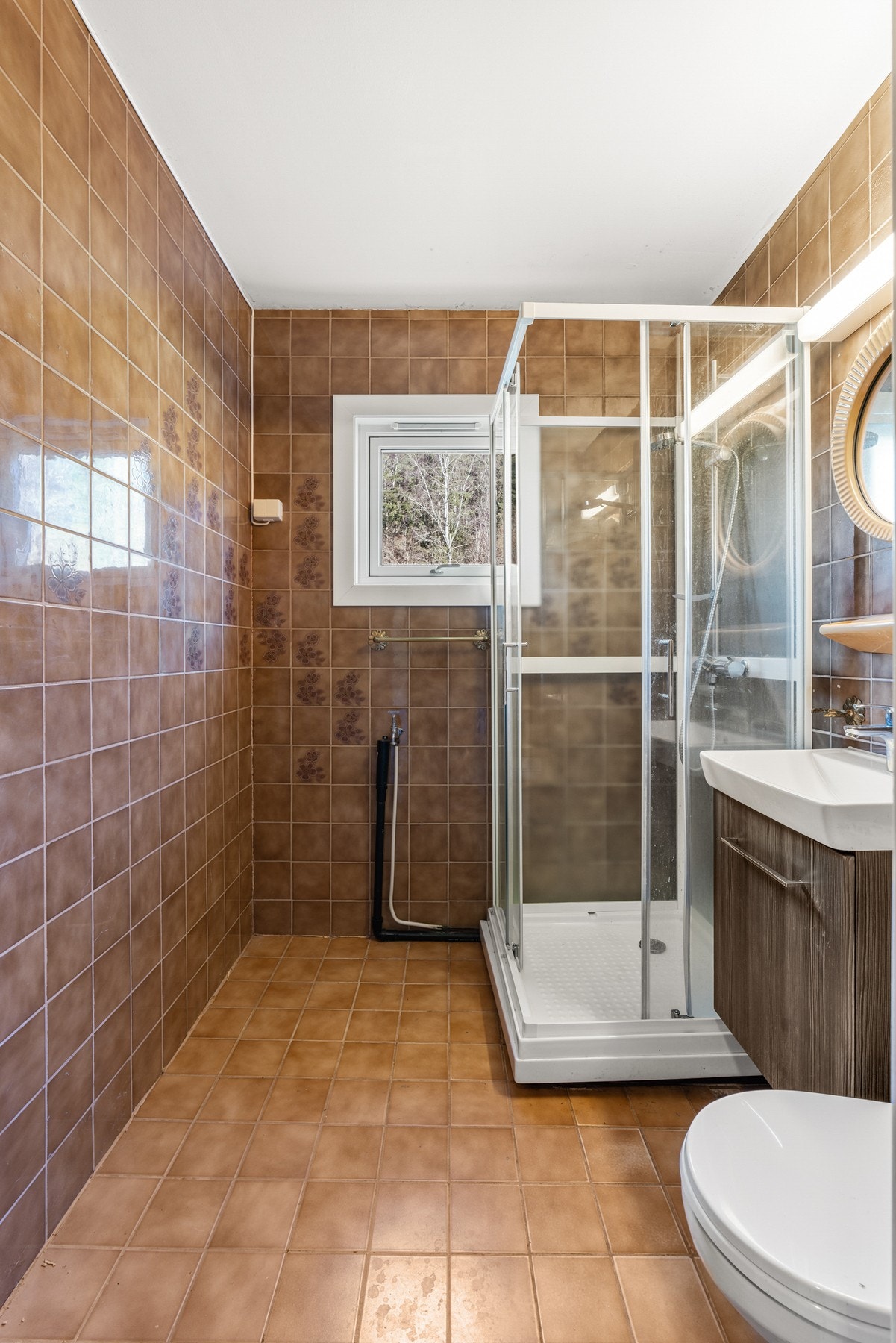 Eldre bad med fliser på gulv og vegger, og dusjkabinett med to skyvbare glassdører. Galleribilde