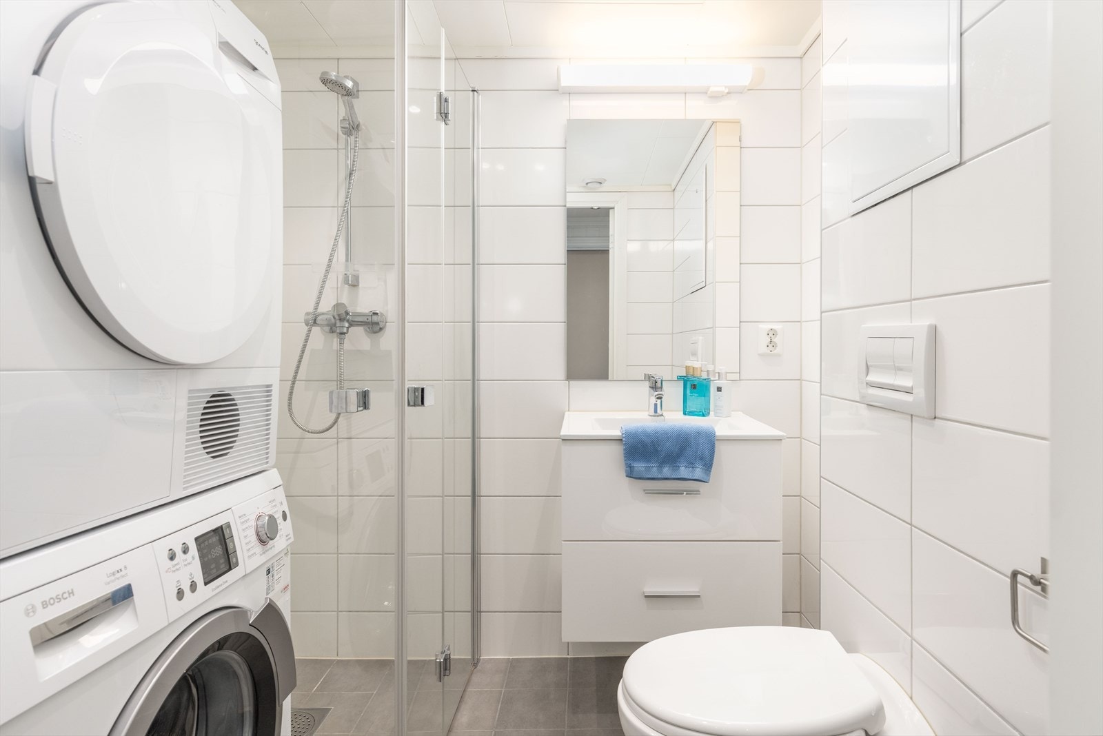 Flislagt bad innredet med heldekkende servant, vegghengt toalett. dusj med innfellbare dører og opplegg for vaskemaskin og tørketrommel. Galleribilde