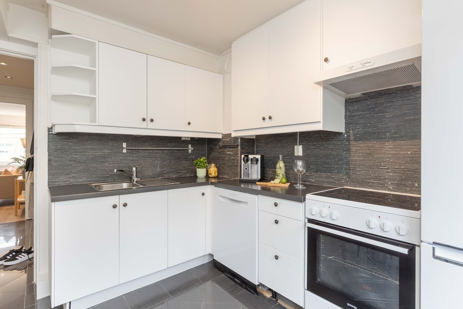 Kjøkkeninnredning fra IKEA med malte fronter, benkeplate av laminat, fliser over benkeplate og belysning/stikk under overskap. Galleribilde