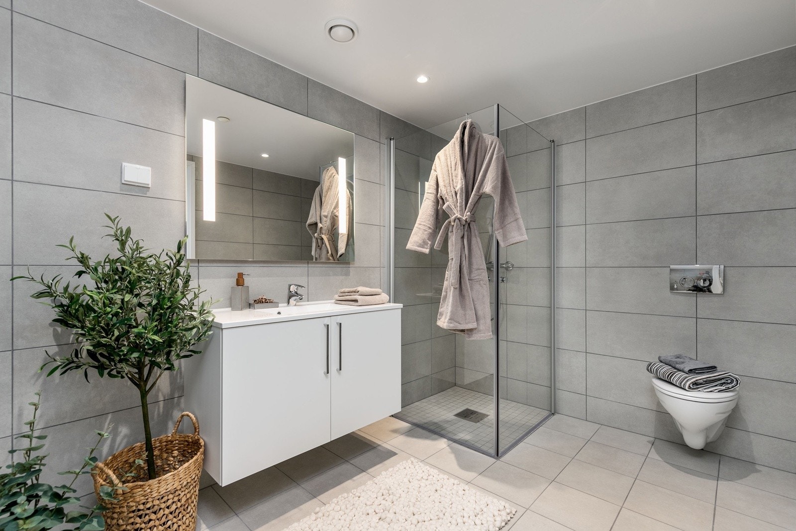 Delikat flislagt bad med vegghengt toalett, dusjsone med innfellbare dører samt servant med skapinnredning. Galleribilde