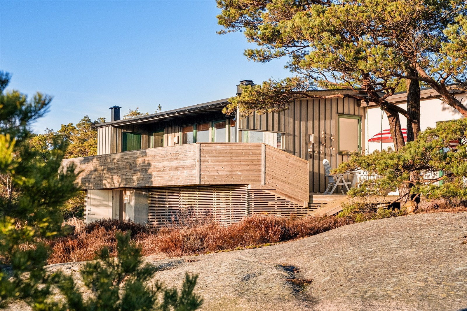 Rekkverk, spiler og trapper i umalt trevirke spiller på lag med de naturlige omgivelsene og gjør hytta mindre fremtredende i terrenget. Galleribilde