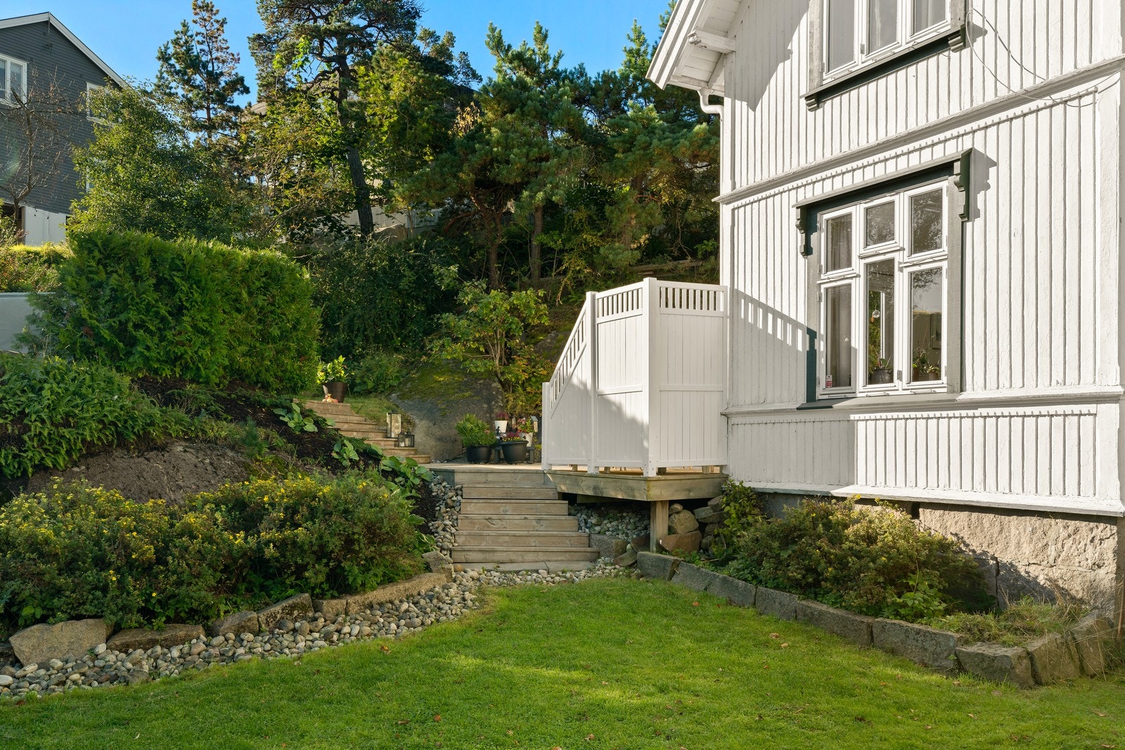 Tomten er opparbeidet med gressplen, trær og busker, samt steinlagt gangvei. Galleribilde