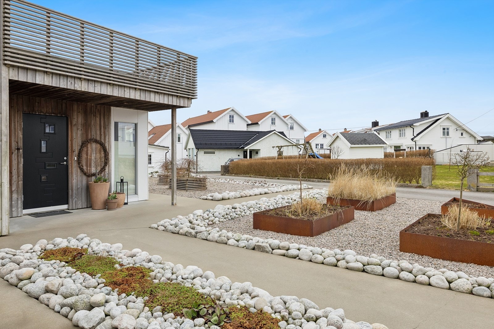 Innbydende inngangsparti med pent opparbeidede utearealer, dekorativ steinsetting og beplantede bed. Galleribilde