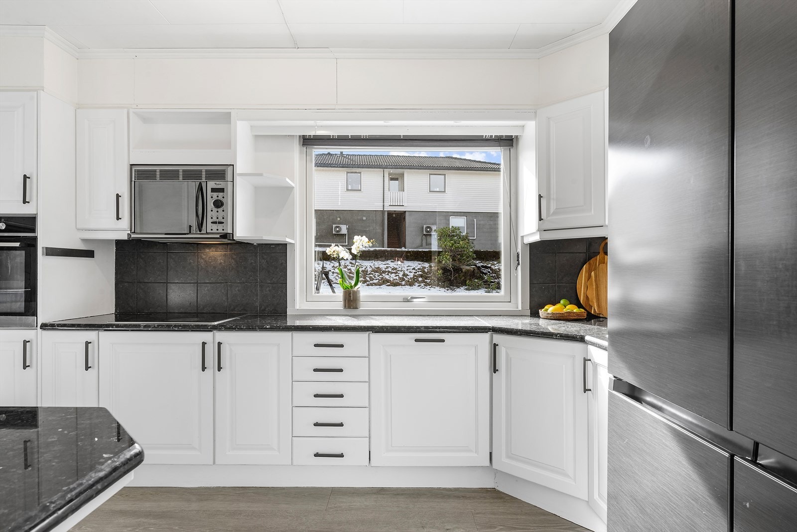 Hvit kjøkkeninnredning med profilerte fronter og benkeplate i stein gir et stilrent utseende. Galleribilde