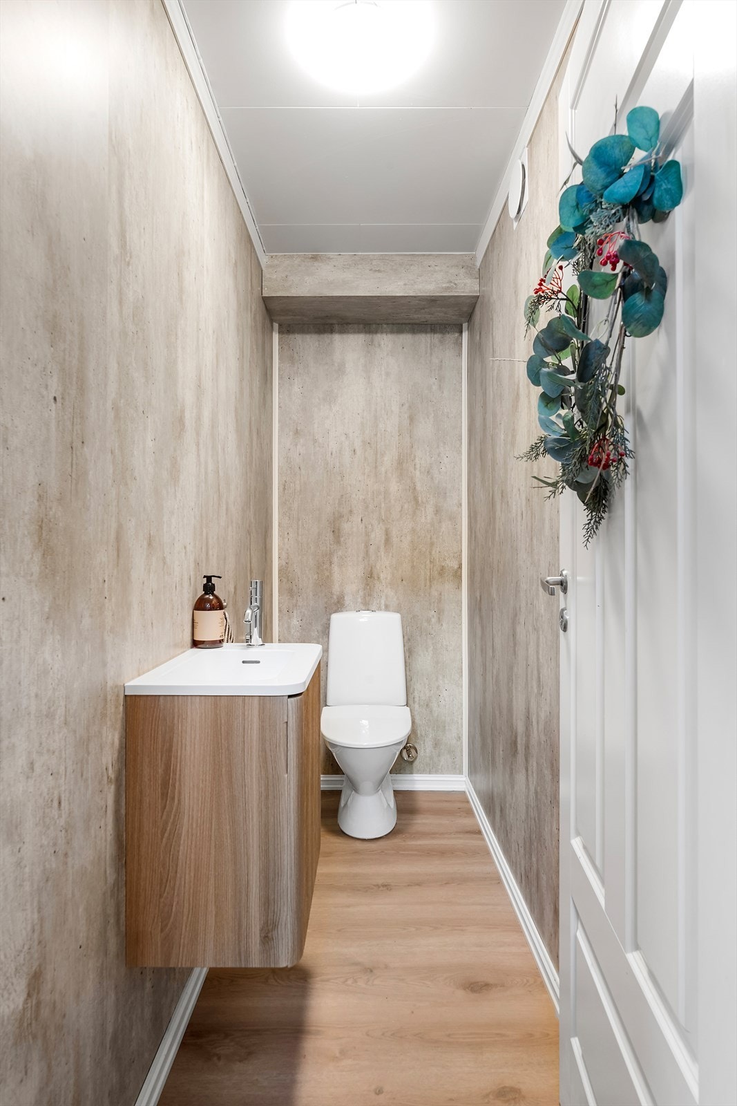 Toalettrommet har laminatgulv og vegger kledd med baderomsplater, samt en enkel innredning med servantplate og gulvmontert toalett. Galleribilde