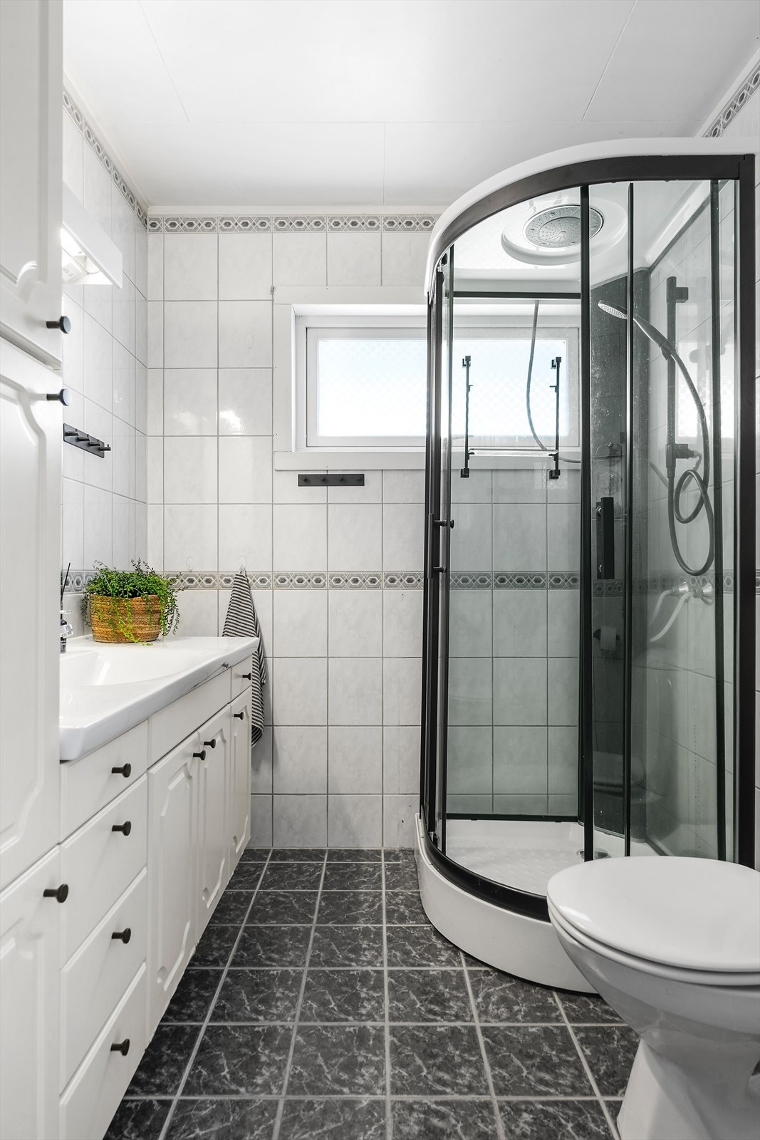 Flislagt bad utstyrt med stor baderomsinnredning, wc og dusjkabinett. Galleribilde