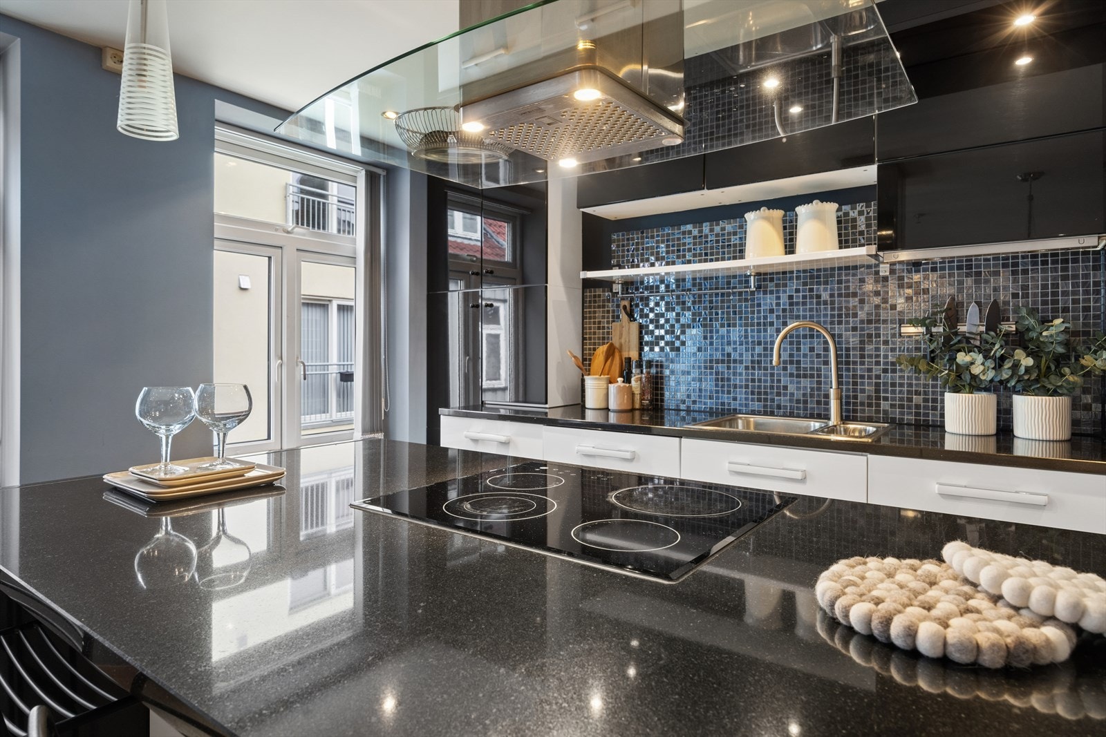 Platetoppen er integrert i kjøkkenøya, med en fritthengende ventilator i stål og glass over. Galleribilde