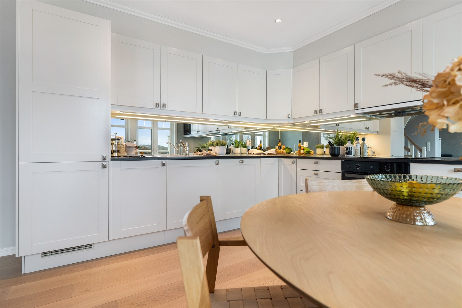 Kjøkkenet har innredning med profilerte fronter og benkeplate av laminat. Speil mellom benk og overskap, reflekterer lyset og skaper en romslig og elegant finish Galleribilde