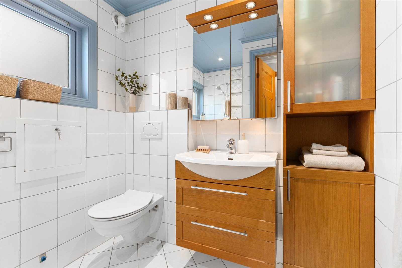 Helfliset bad innredet med servant i møblement, speilskap, belysning og vegghengt skap, vegghengt toalett og dusjhjørne. Galleribilde