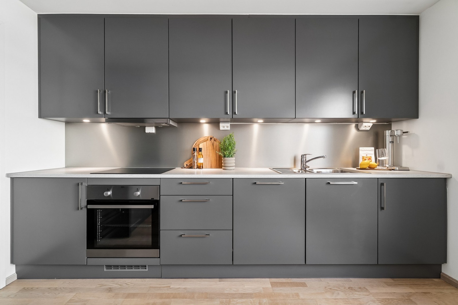 Kjøkkenet gir et stilrent og moderne inntrykk med mørke fronter og en lys benkeplate, samt integrerte hvitevarer og innfelte spotter under overskapene. Galleribilde