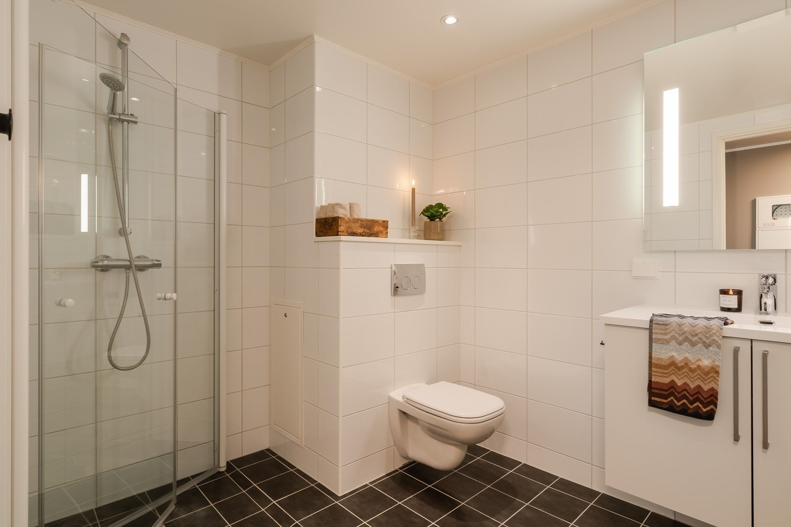 Badet ligger i første etasje og har godt armslag med sine 7,5 kvm. Gulvet er lagt med mørke fliser, mens veggene har hvite fliser. Galleribilde