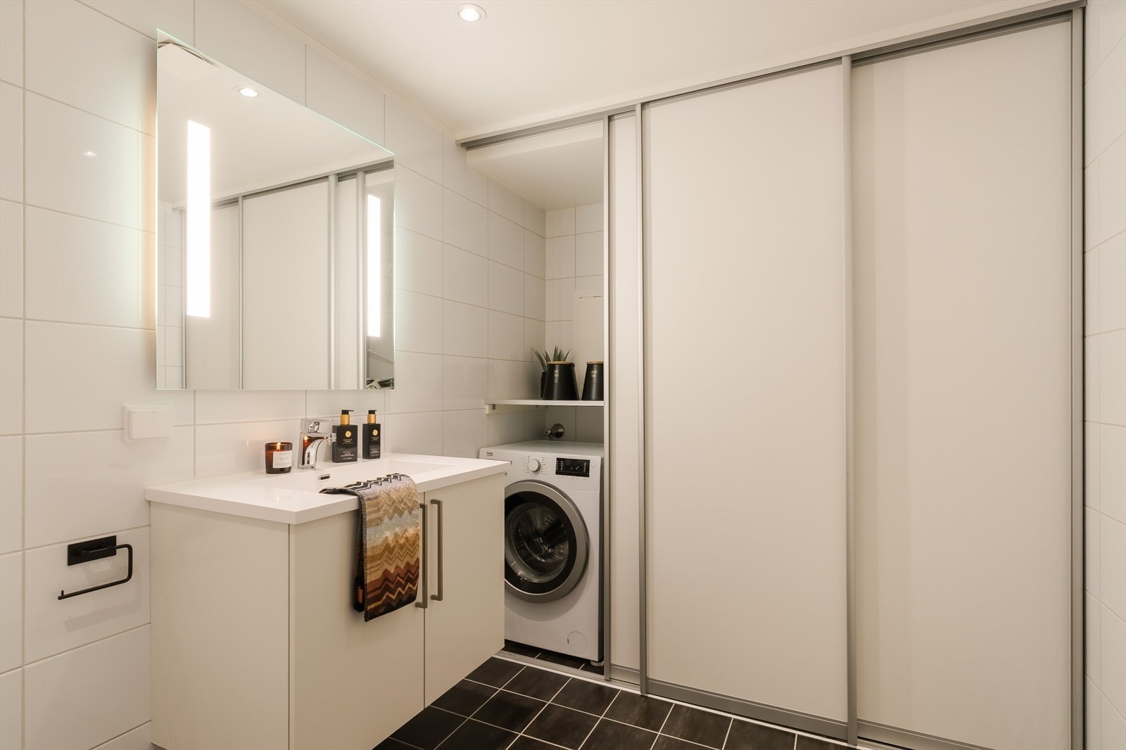 En smart skyvedørsgarderobe gir god oppbevaringsplass samtidig som det skjuler opplegg og plass for vaskemaskin og tørketrommel. Her er det også tilgang på NIBE-enhet som styrer husets varmtvann og ventilasjon. Galleribilde