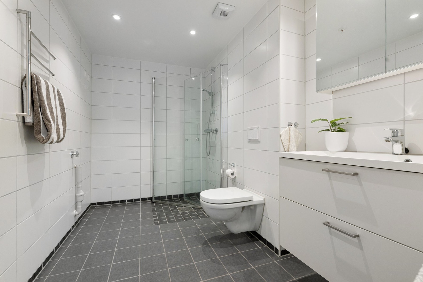 Hovedbadet fremstår som stilrent og moderne, med flislagte overflater, varmekabler og opplegg for vaskemaskin og tørketrommel. Galleribilde