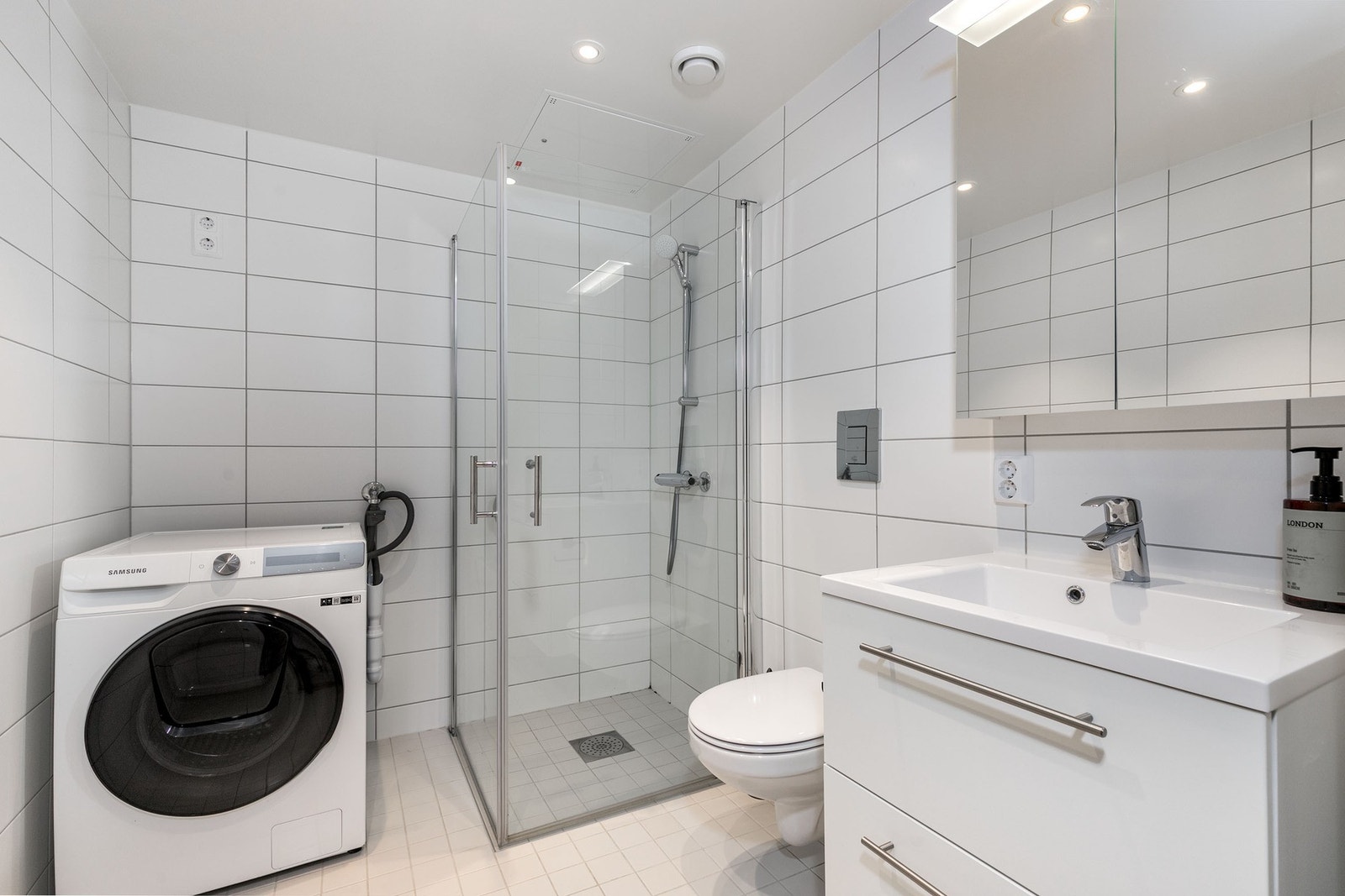 Delikat og tidsriktig bad med flislagte overflater og et rent, tiltalende uttrykk. Badet er innredet med vegghengt servantskap med heldekkende servant, speilskap med integrert belysning og vegghengt toalett. Dusjhjørne med innfellbare glassdører gir en el Galleribilde