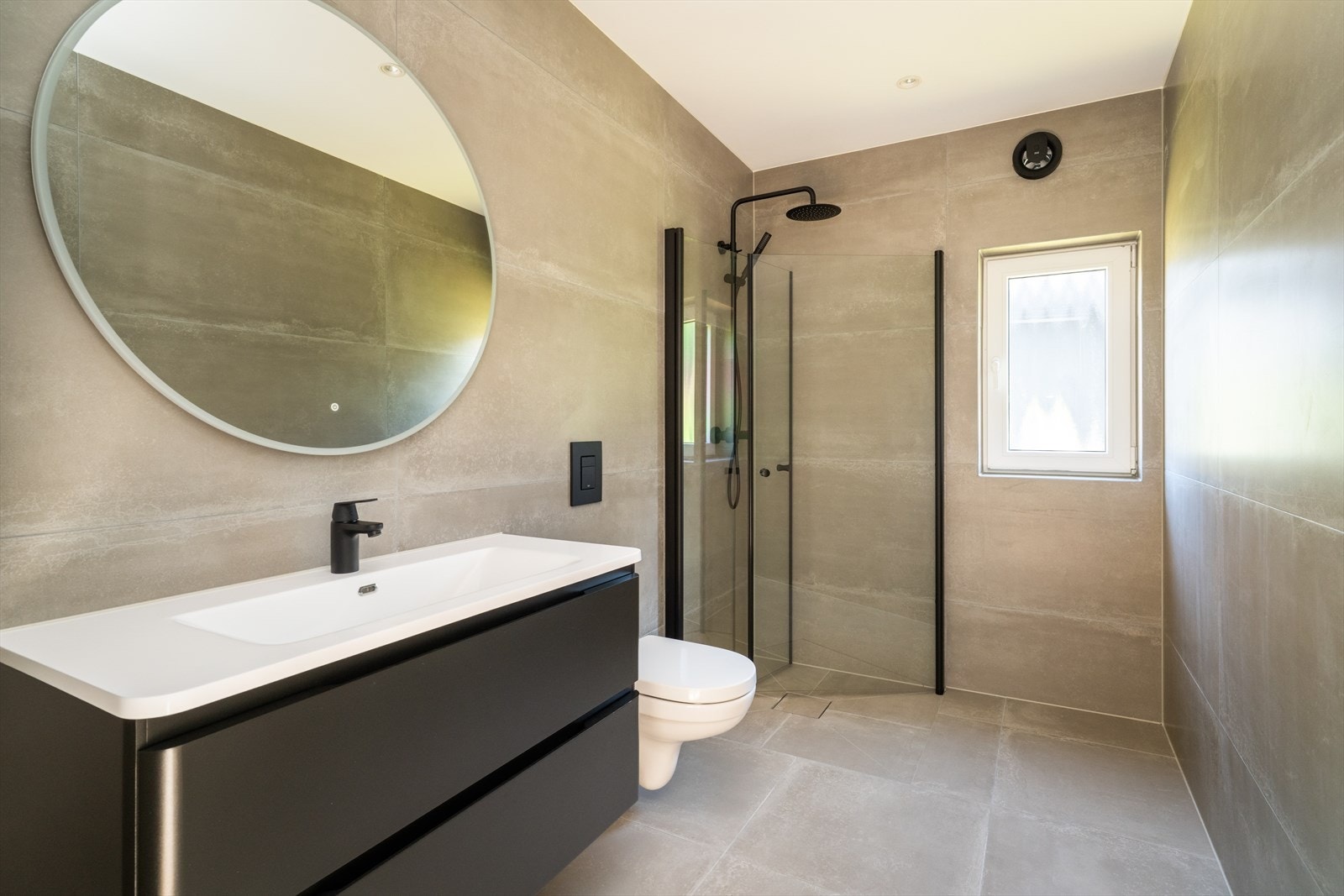 Delikat baderom med heldekkende servant med underskap, speil med lys, veggmontert toalett og dusjhjørne. Galleribilde