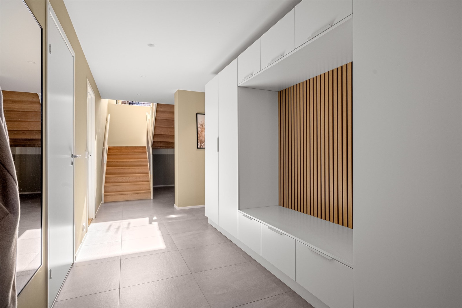 Romslig entré med flotte fliser på gulv, varmekabler og malte vegger. Praktisk og stilig nisje med benk i vegg med spilevegg, praktisk når man skal ta av og på sko. Det er skap til oppbevaring som rammer inn nisjen. Galleribilde