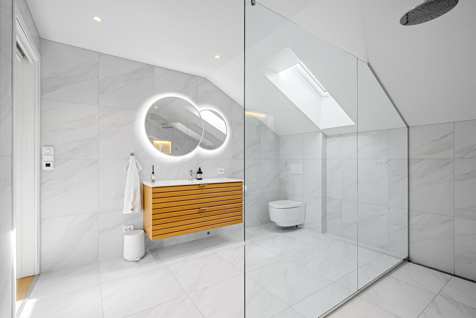 Lyse fine fliser på gulv og vegg, romslig dusjnisje med glassvegg, vegghengt toalett og servant med skuffer. Store speil på vegg. Varme i gulv og spotter i tak. Galleribilde