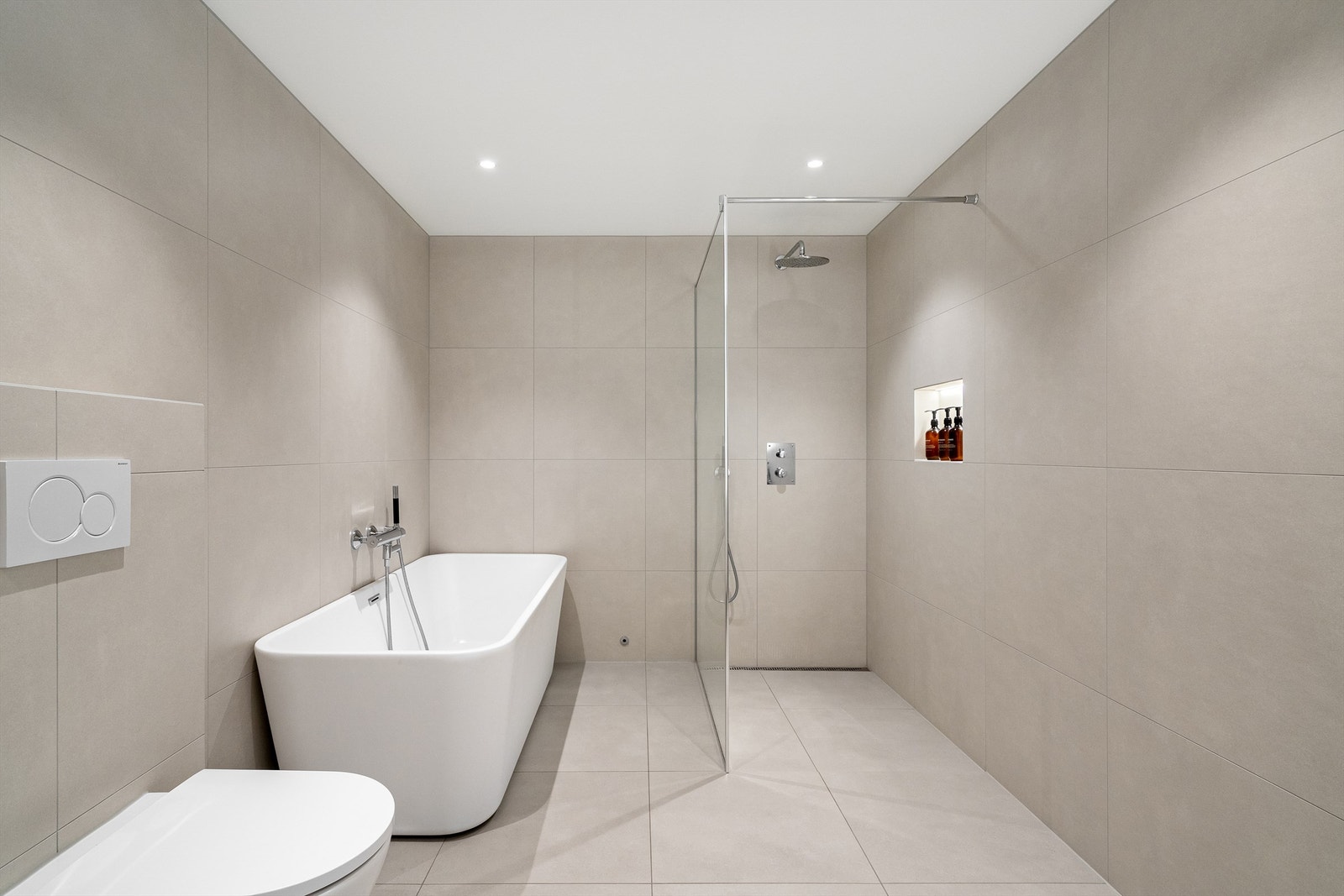 Det er fine lyse fliser, stor dusjnisje med glassvegg, badekar og servant med skuffer. Stort speil på vegg, spotter i tak. Galleribilde