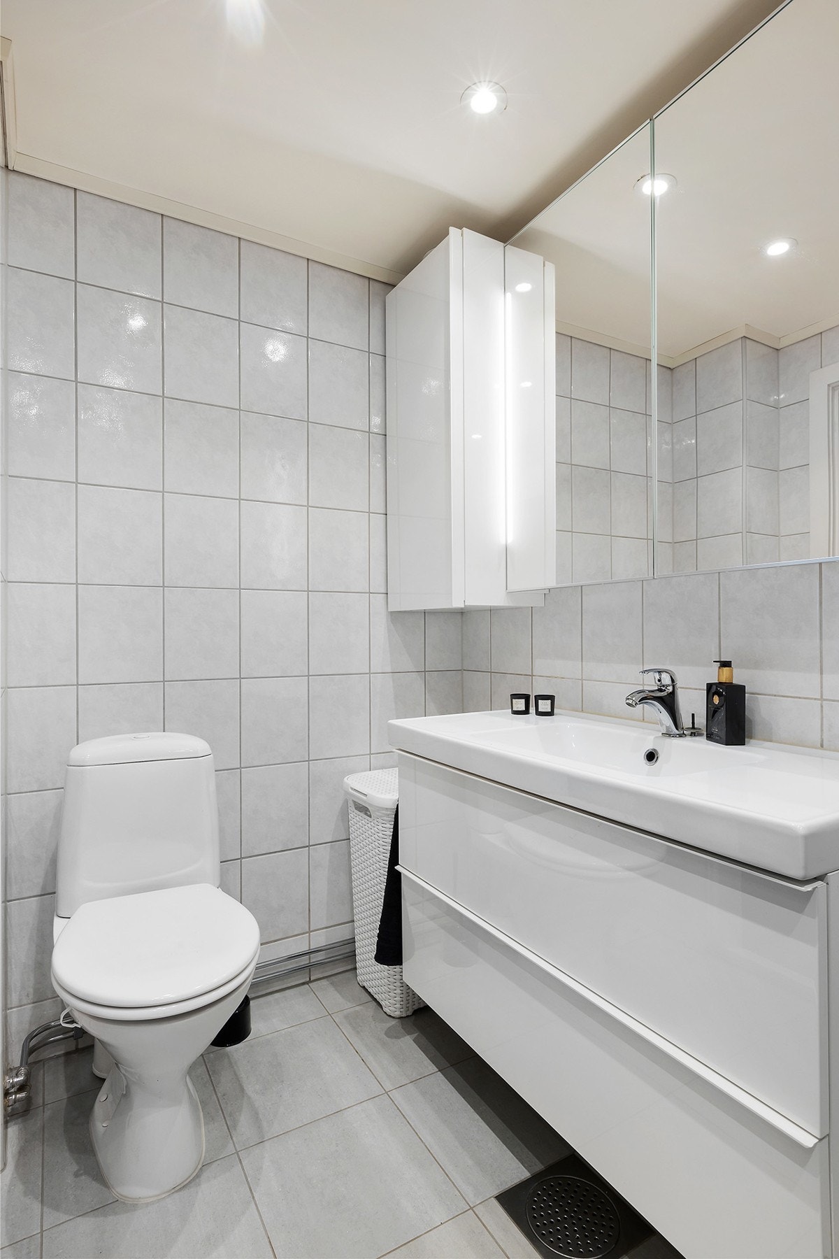 Badet er utstyrt med servant med skuffeseksjon, speilskap med sidelys, gulvmontert klosett, veggskap og dusjhjørne med svingbare glassdører. Opplegg for vaskemskin. Galleribilde