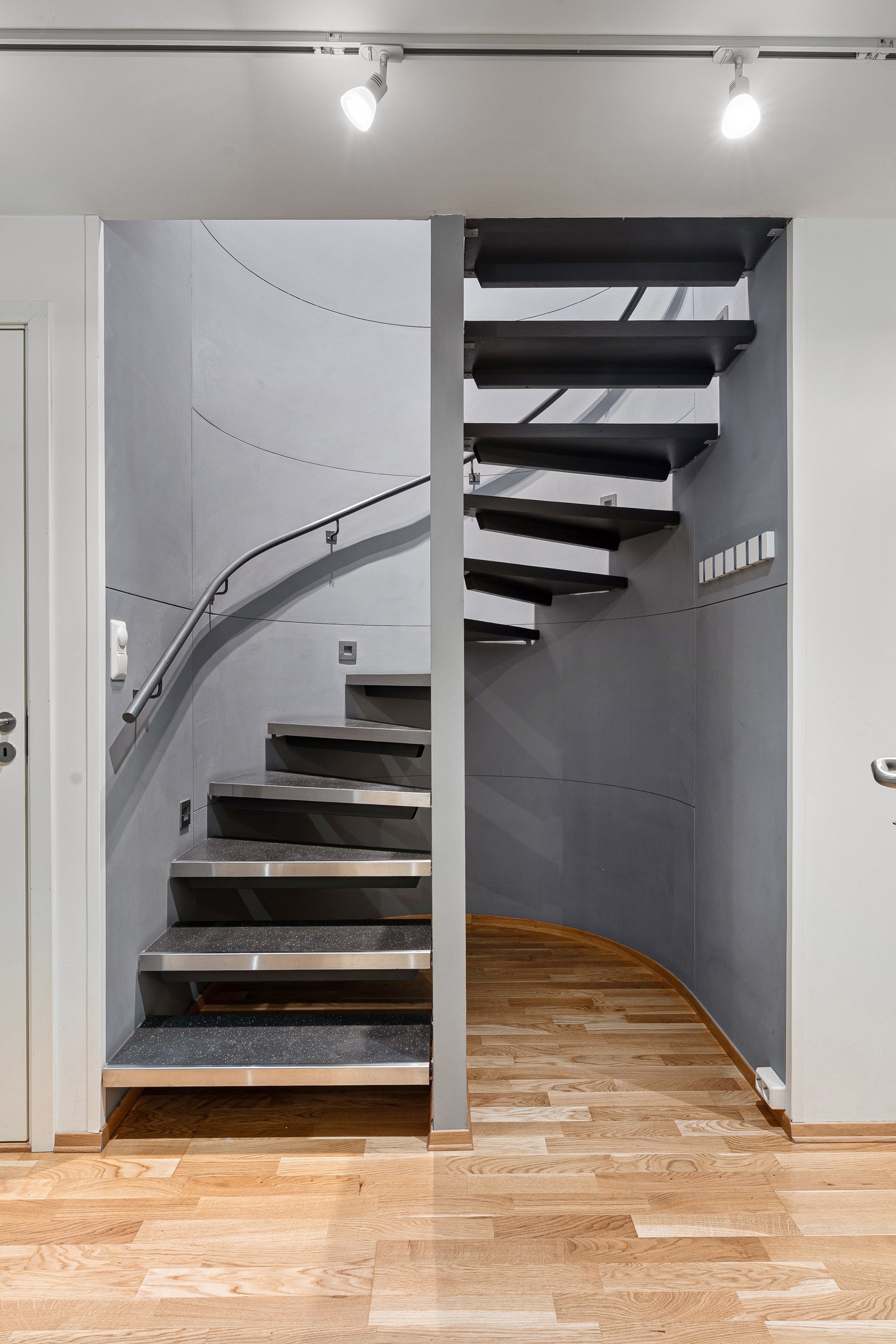 Romslig gang/trapperom i første plan med parkettgulv og malte veggoverflater