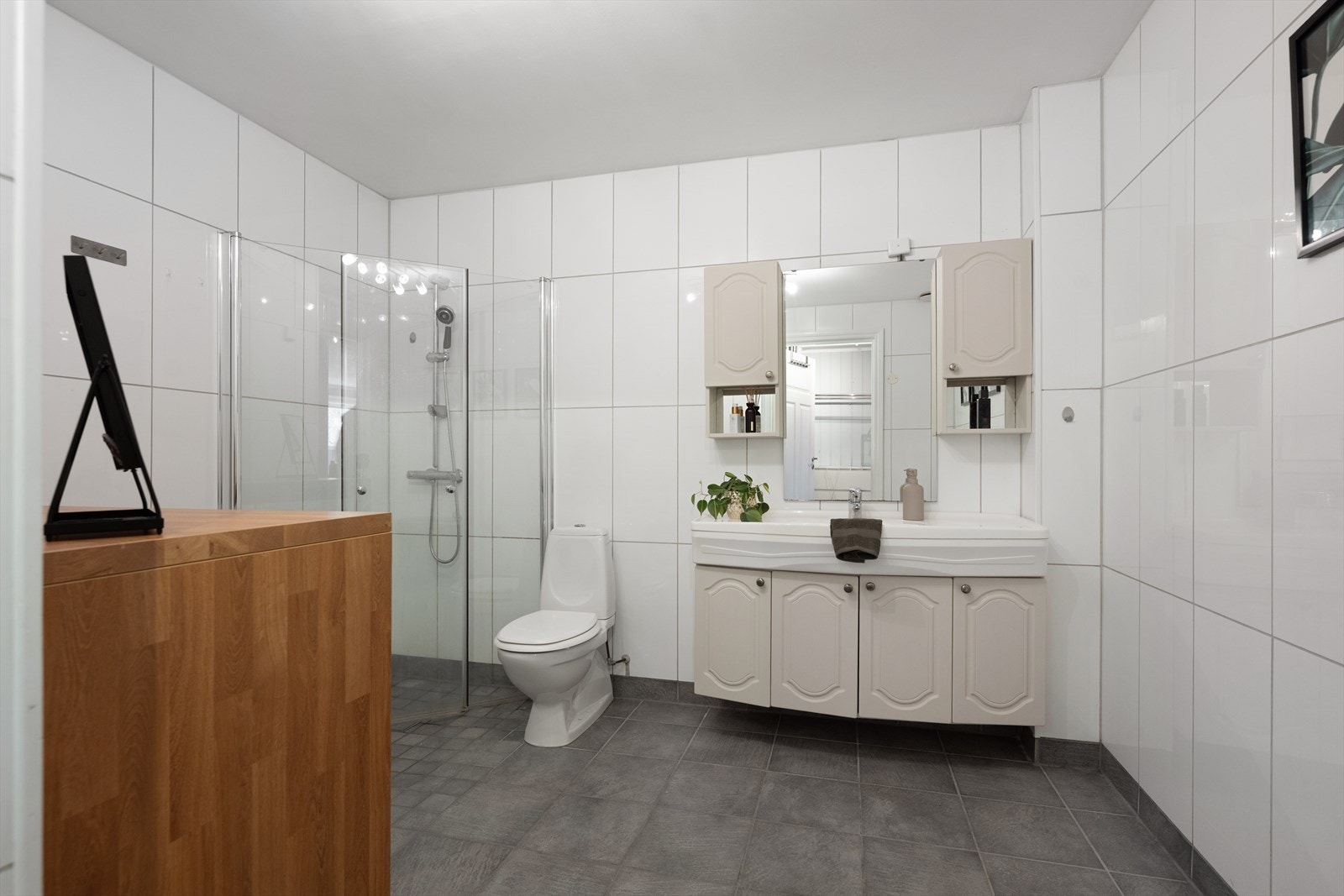 Badet er flislagt på gulv og vegger, og det er varme i gulvet. Innredningen består av servantskap med nedfelt servant, samt veggskap med speil. Det er gulvmontert klosett og en romslig dusjsone med innfelte dusjdører i herdet glass. Galleribilde