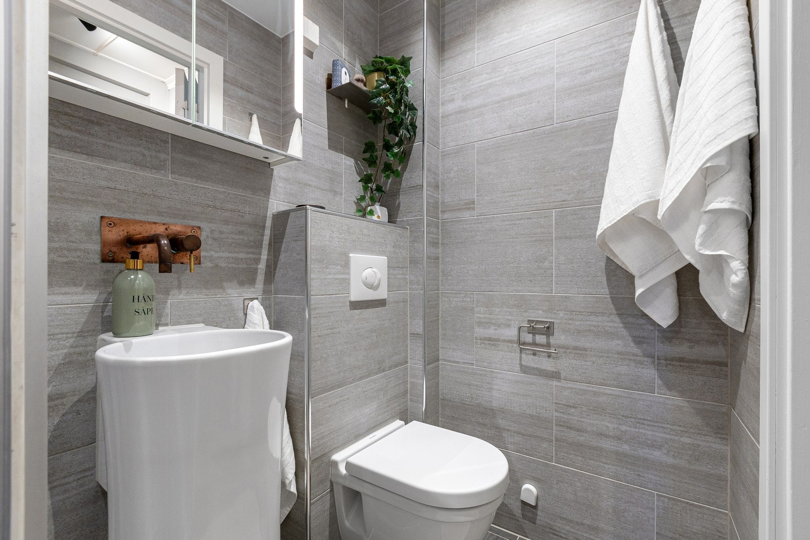 Videre er badet innredet med med vegghengt servant, speilskap med belysning og vegghengt toalett. Galleribilde