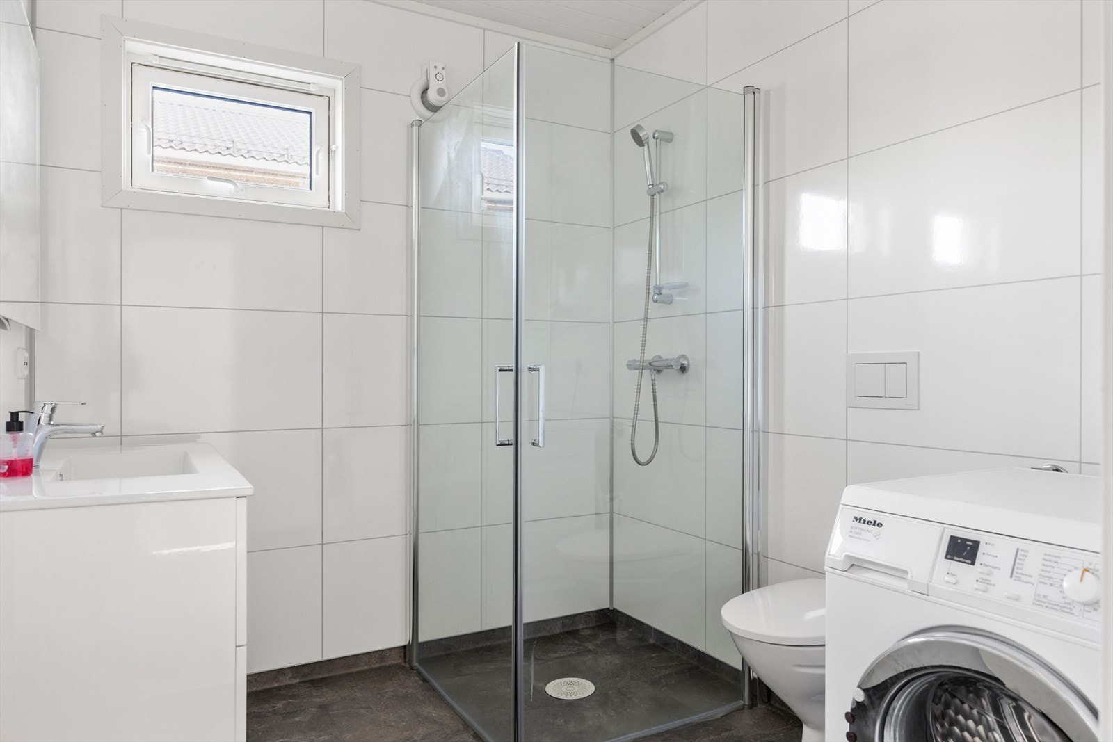 Lyst og moderne bad med dusjkabinett, wc, servant og opplegg for vaskemaskin. Galleribilde