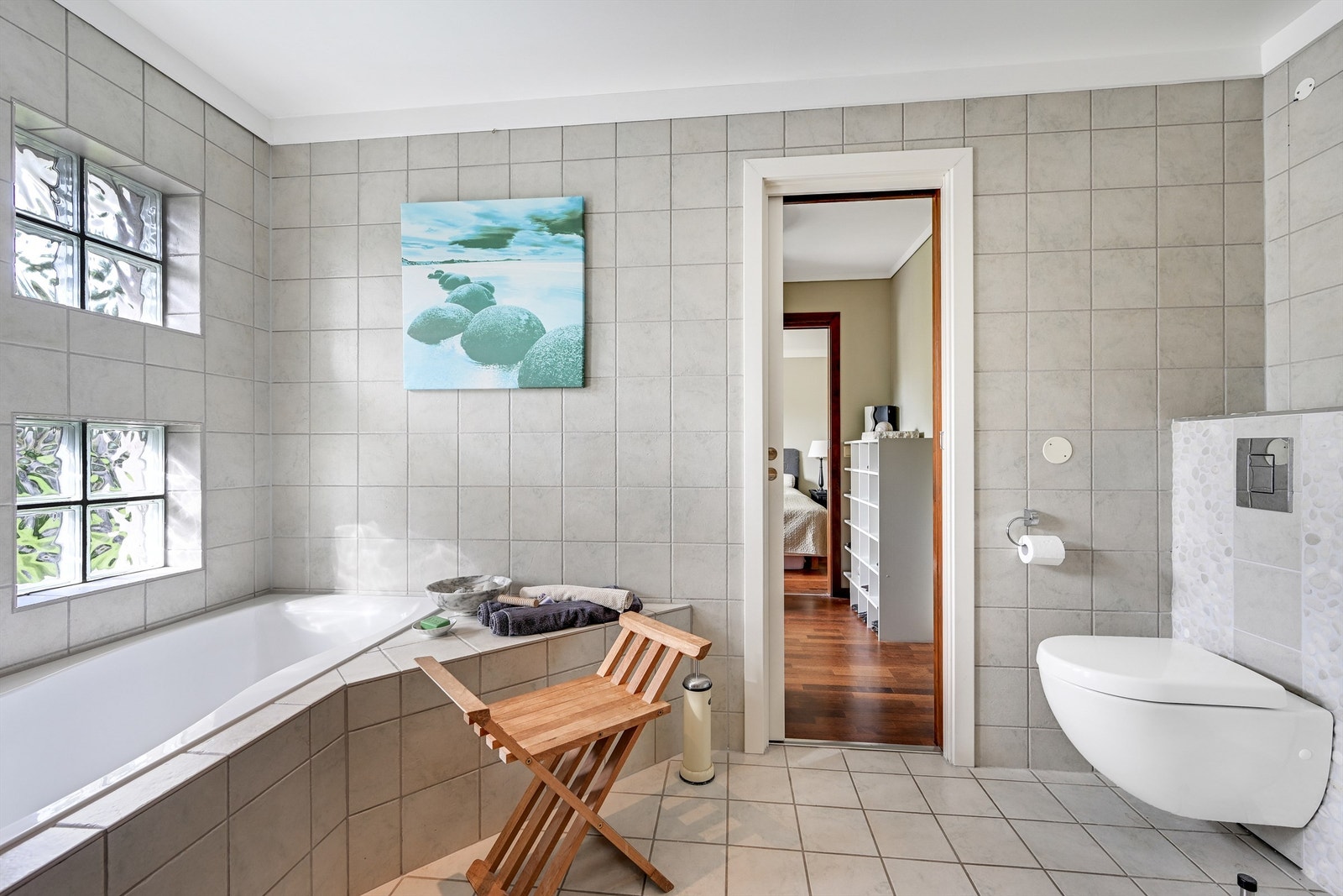 Badet er innredet med dusjnisje med glassdør inn til dusjsonen, vegghengt toalett, innbygget badekar og servant montert i baderomsinnredning. Galleribilde