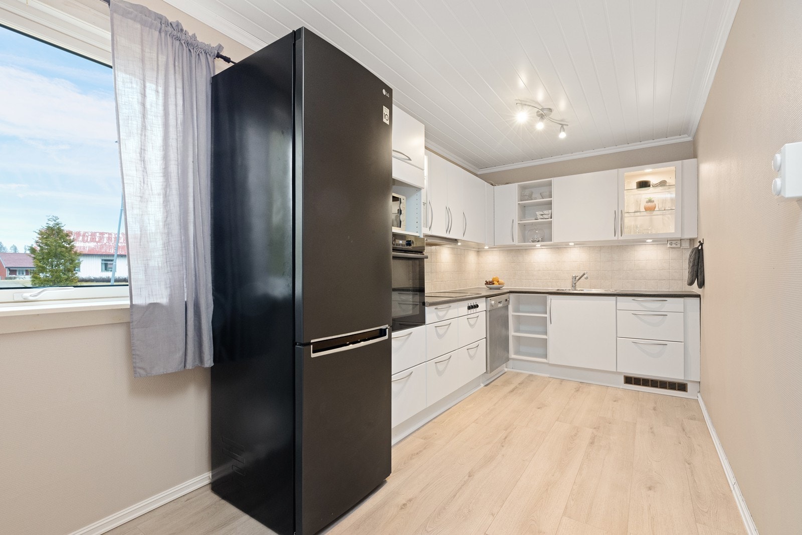 Kjøkkenet har slette, lyse fronter og laminerte benkeplater med integrerte hvitevarer som komfyr og platetopp. Galleribilde