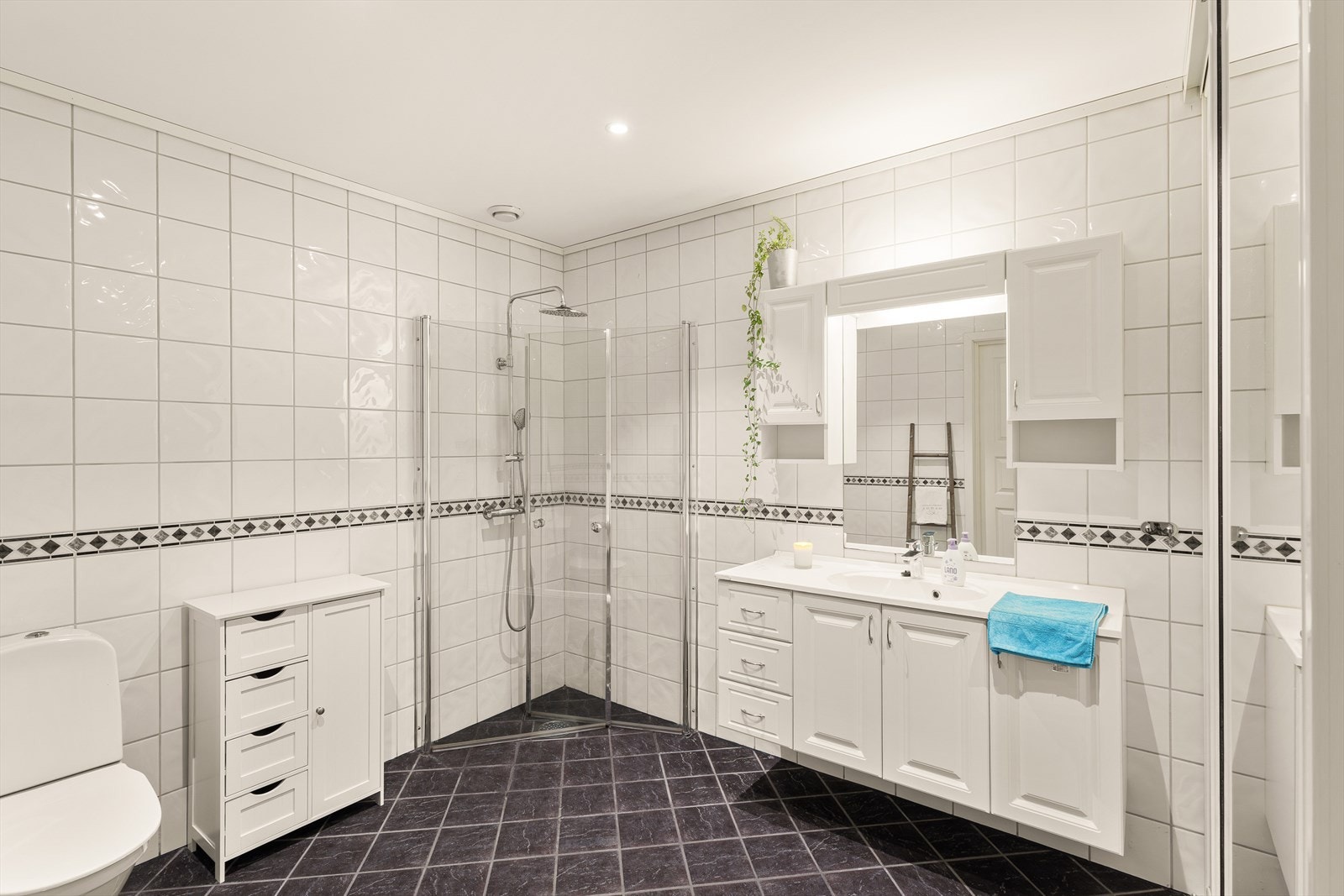 Badet er pent innredet med servant med møblement, speil med belysning, toalett og dusjhjørne Galleribilde