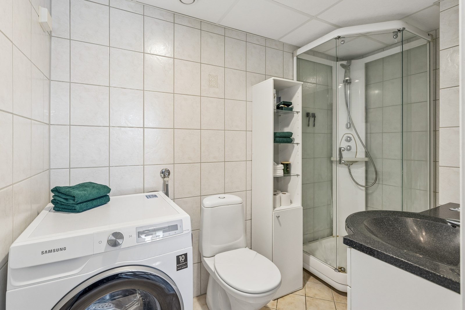 Baderommet har flislagte overflater og er utstyrt med dusjkabinett, servant med innredning og opplegg for vaskemaskin. Galleribilde