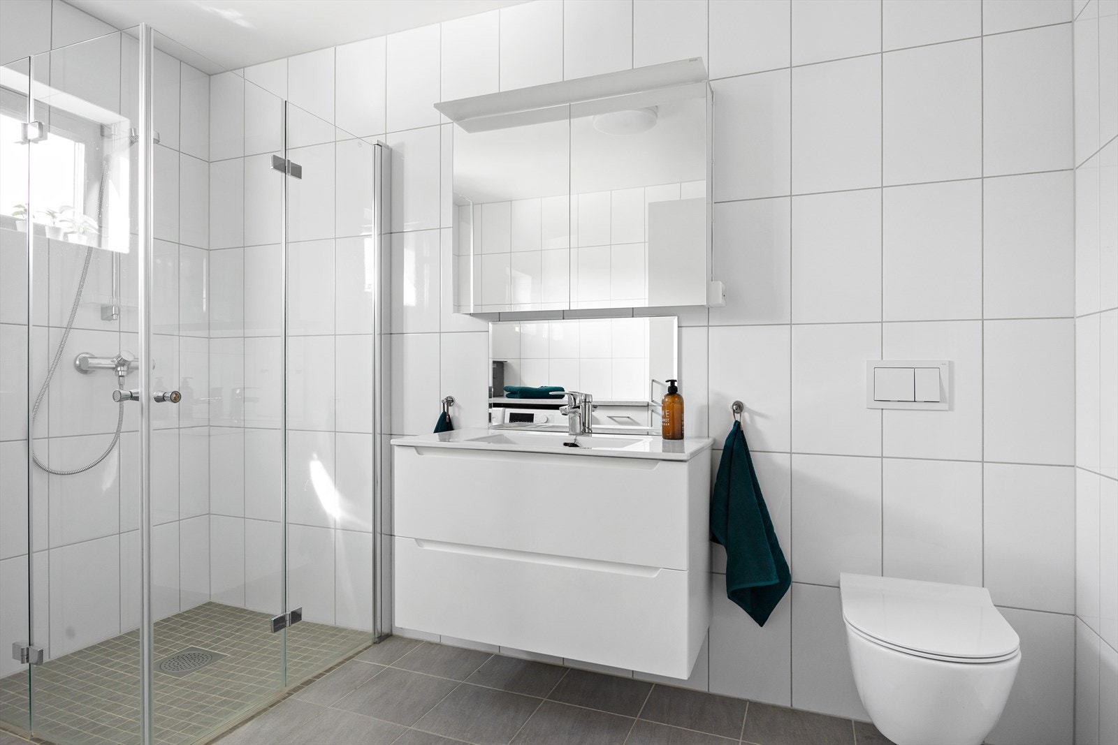 Lyst og helfliset bad som byr på både estetikk og funksjonalitet. Med moderne innredning, vegghengt toalett og dusjhjørne med glassdører, har badet et tidløst preg. Galleribilde