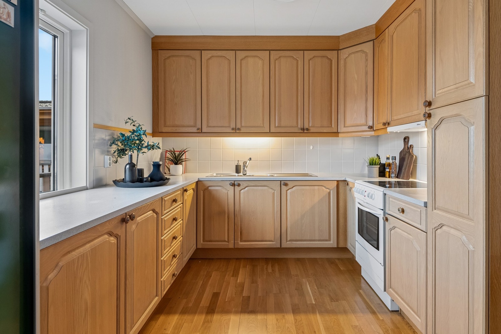 Kjøkkeninnredning med profilerte heltre fronter og benkeplate med vask. Avsatt plass til komfyr og kjøleskap. Galleribilde