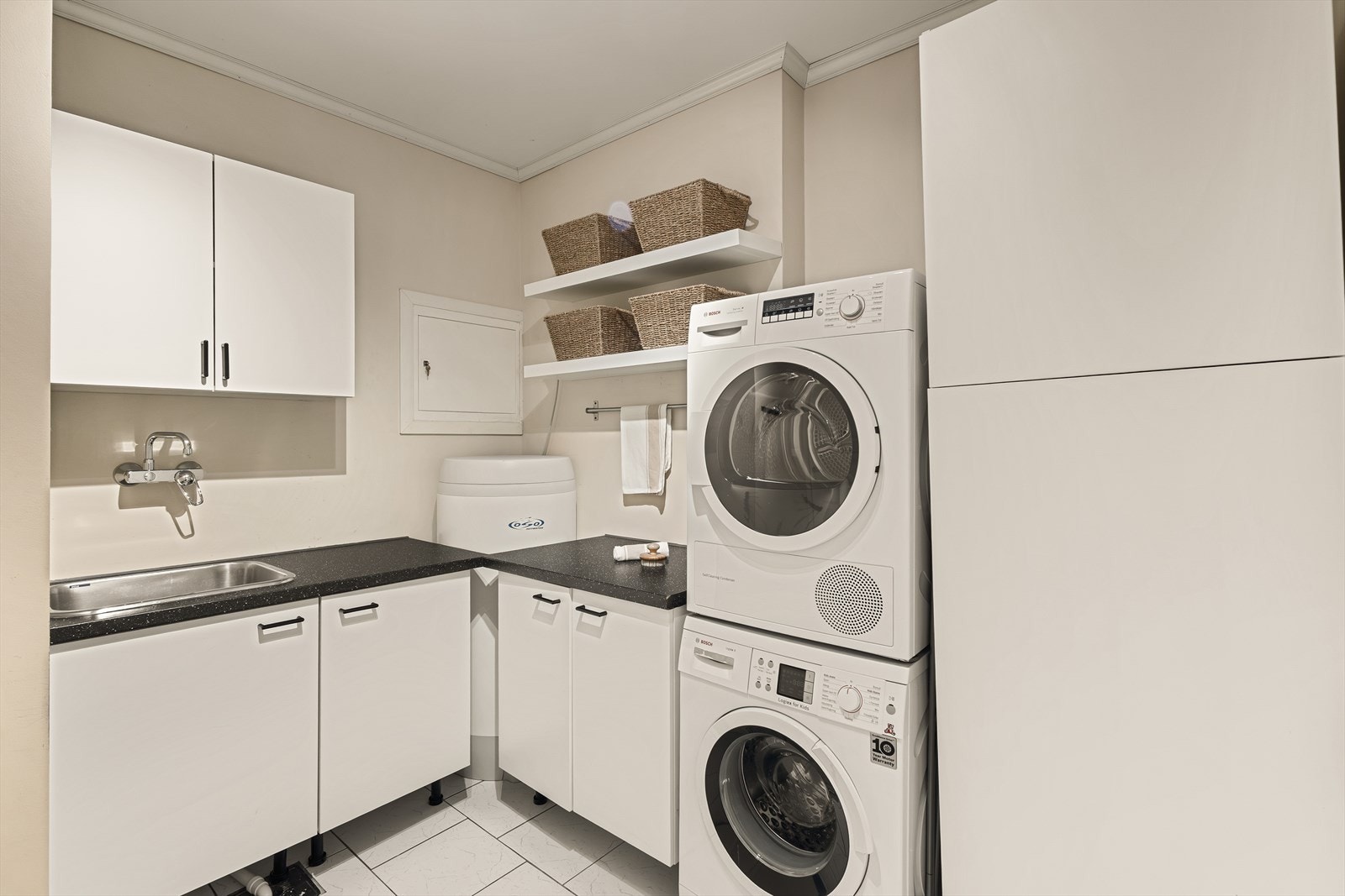 Separat og praktisk vaskerom med gode løsninger for klesvask og oppbevaring. Veggene har malt platekledning, taket har himlingsplater og gulvet er flislagt. Galleribilde