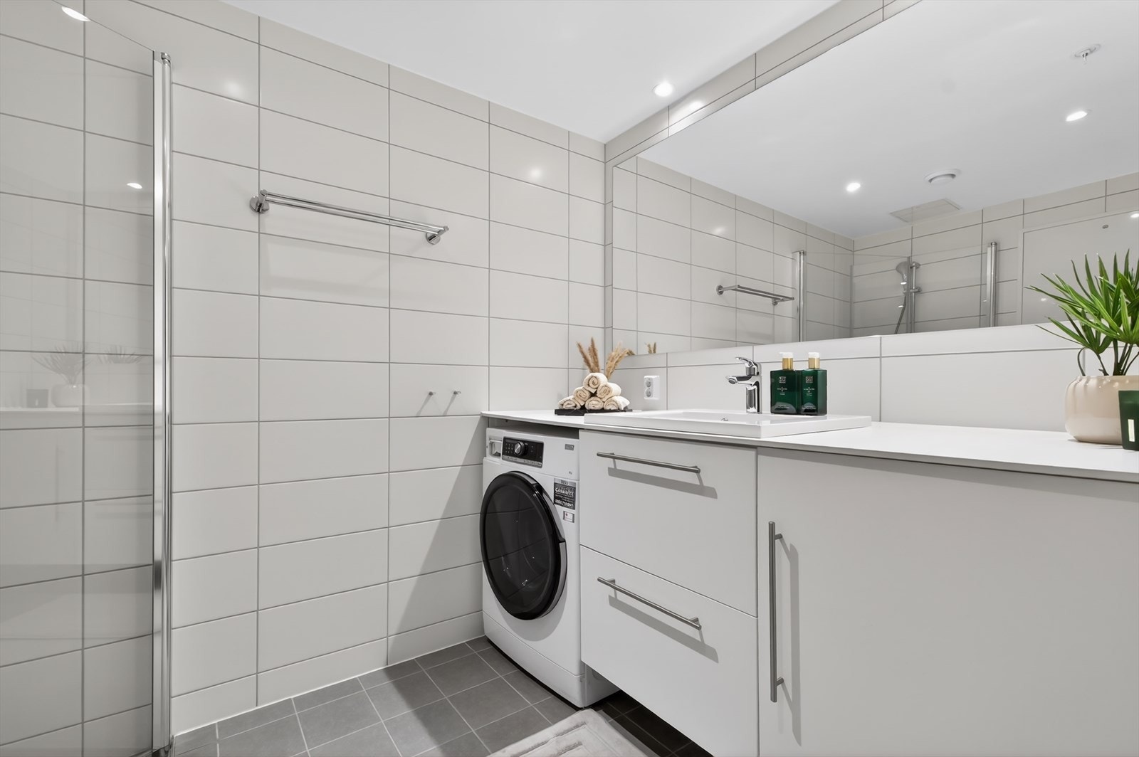 Vegghengt toalett med innebygd sisterne og synlig lekkasjespalte. Gulvet er flislagt med vannbåren gulvvarme, og veggene er kledd med fliser. Nedsenket himling med downlights gir et moderne uttrykk. Galleribilde