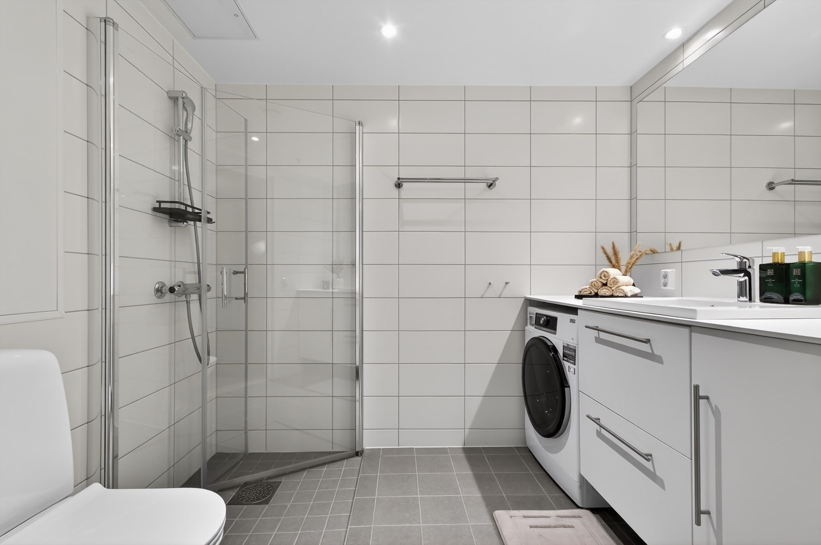 Delikat, flislagt baderom med moderne innredning bestående av servantseksjon med hvite, glatte fronter, heldekkende laminert benkeplate og nedfelt servant. Badet er utstyrt med ettgreps armatur, speil og downlights. Galleribilde