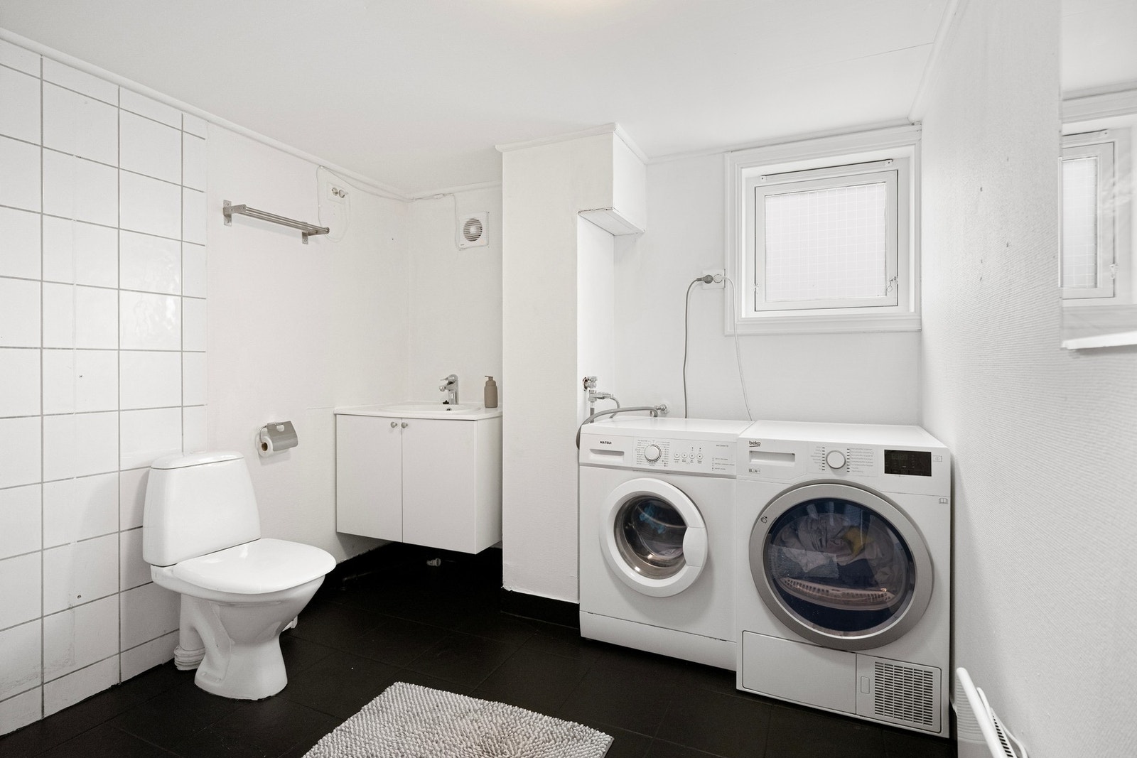 Badet er utstyrt med vegghengt baderomsmøbel med servant, frittstående toalett og opplegg til vaskemaskin. Galleribilde