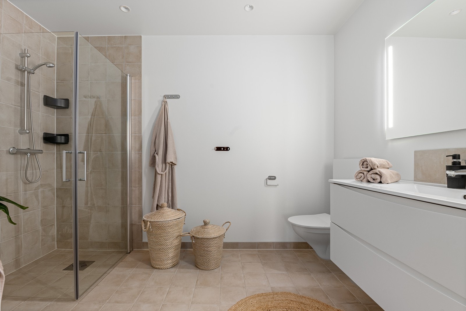 Rommet har innredning med nedfelt servant, skap, fordeler skap for vann, veggmontert toalett og dusj med hjørnevegger. Gulvet er flislagt og utstyrt med elektriske varmekabler, som gir komfort og en lun atmosfære. Galleribilde