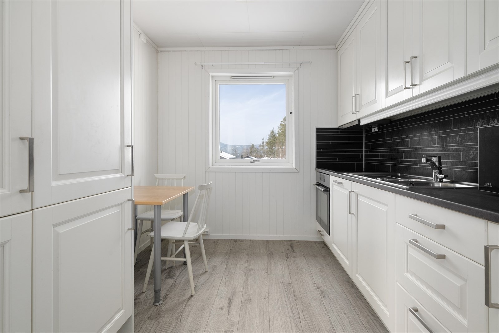 Kjøkkenet har en pen og takhøy innredning fra 2022 med profilerte fronter, laminat benkeplate og beskyttelsesplater over kjøkkenbenk. Det er ventilator med avtrekk ut og integrerte hvitevarer som kjøl/ fryseskap, oppvaskmaskin, platetopp og stekeovn. Galleribilde