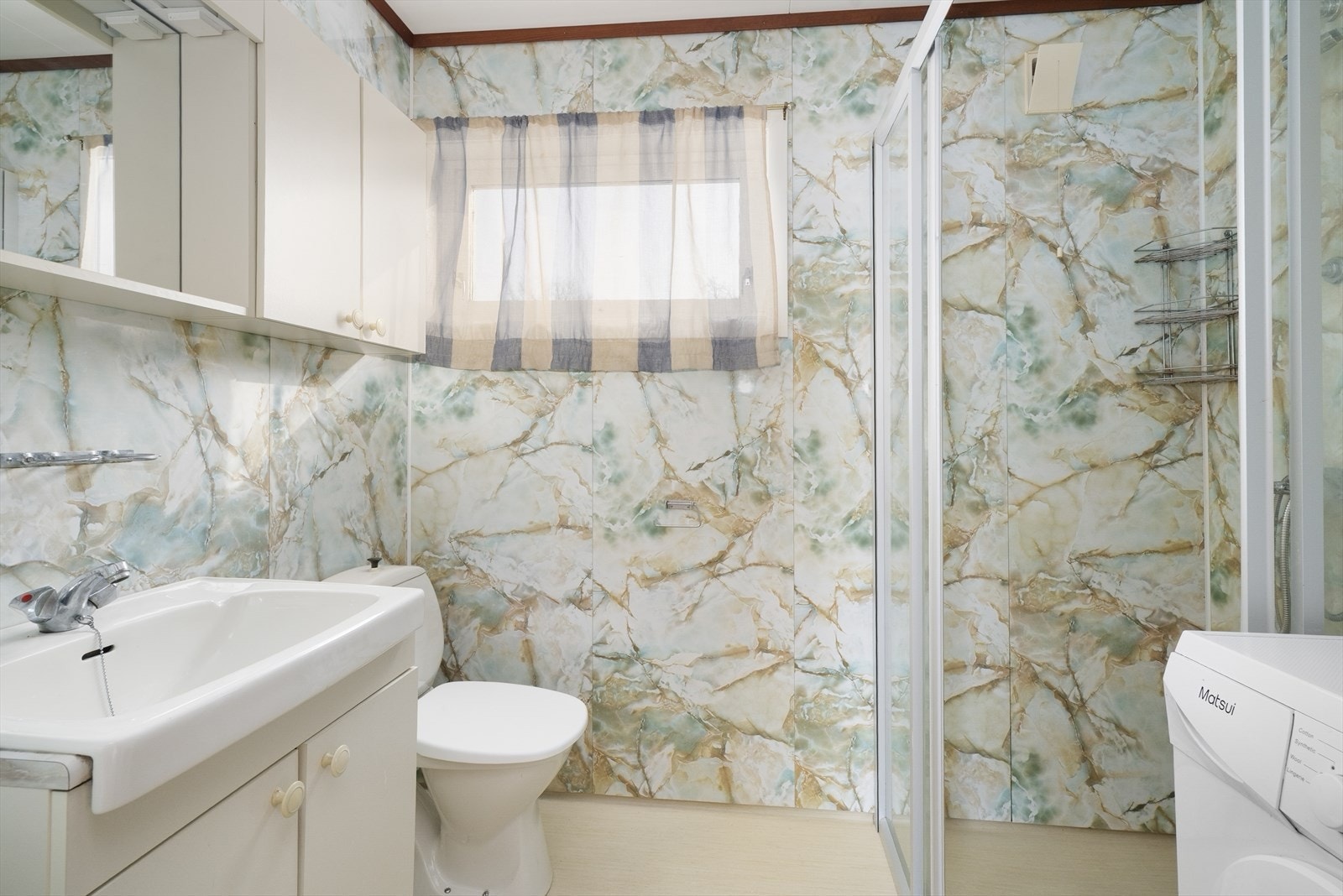 Bad fra 1983 med belegg på gulv og baderomsplater på vegger. Badet har dusjhjørne, toalett og innredning med heldekkende vask, under- og overskap med slette fronter og speil. Varmekabler, opplegg for vaskemaskin og ventilasjon via ventil i tak. Galleribilde