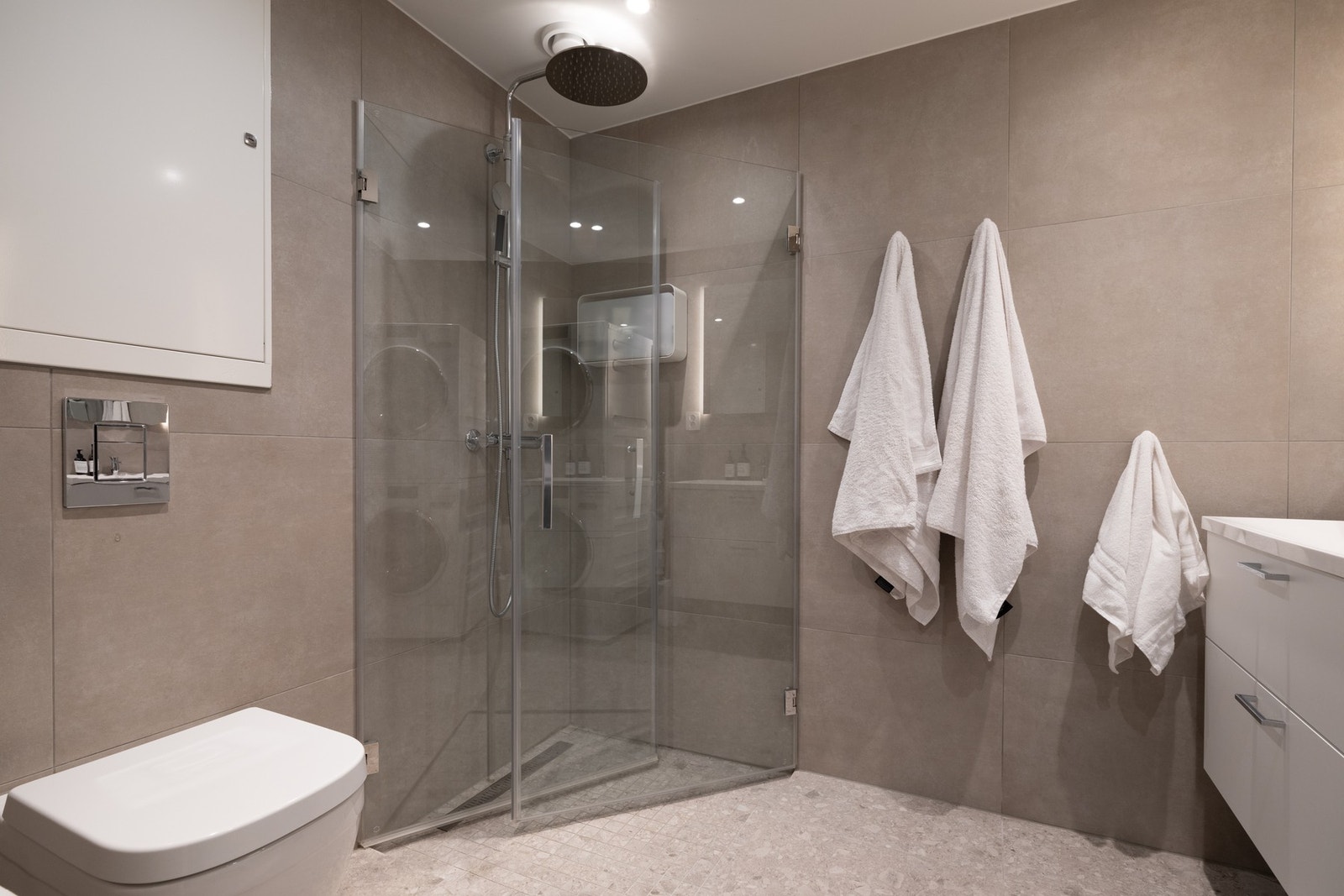 Flislagt og moderne baderom. Dusjhjørne med innfellbare dører, dusjdører med beslag i krom, regnfallsdusj fra Mora og slukrenne Galleribilde