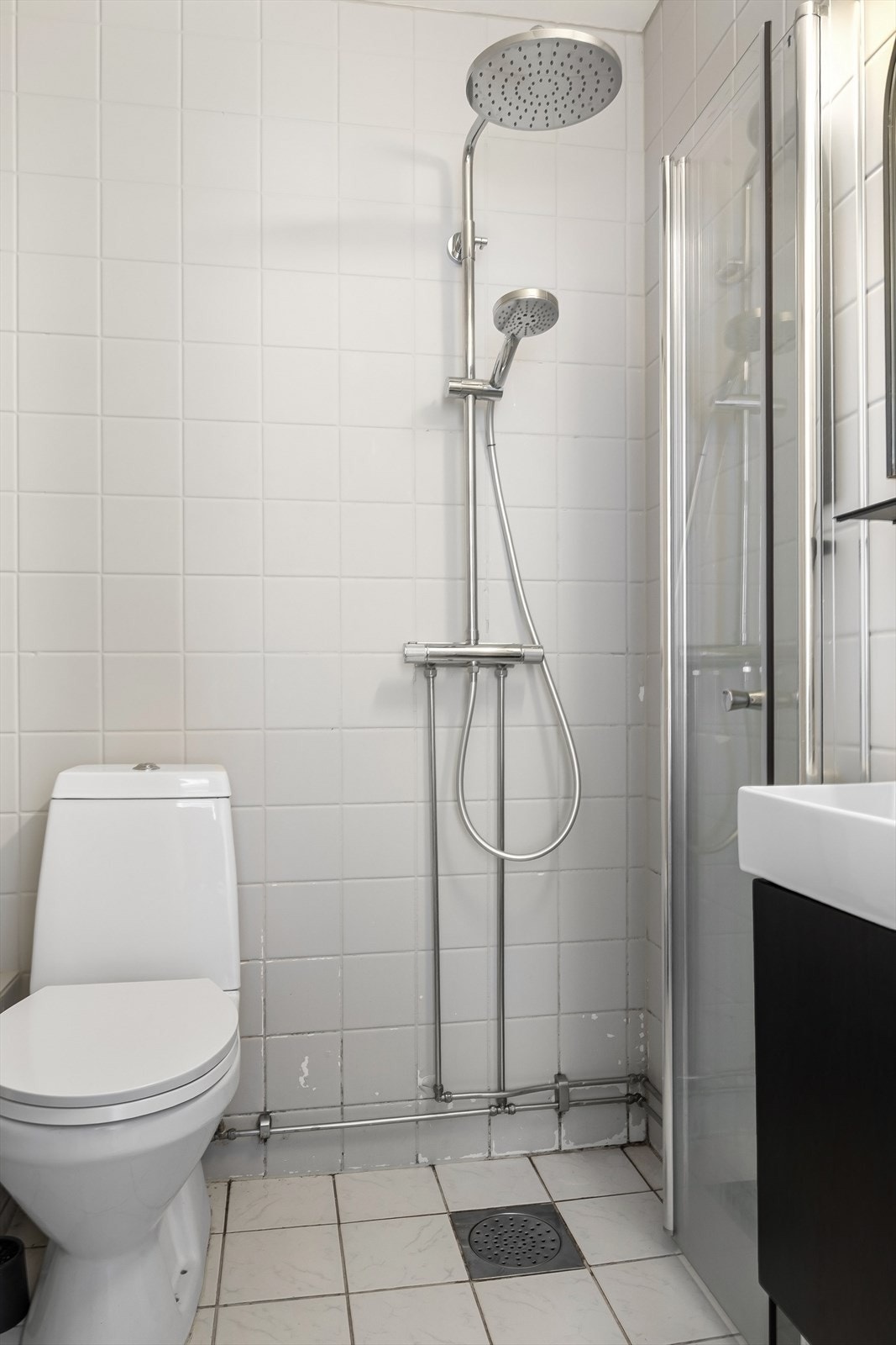 Innredet med regnfalldusj og innfellbar dør i herdet glass, servant, klosett og opplegg for vaskemaskin. Galleribilde