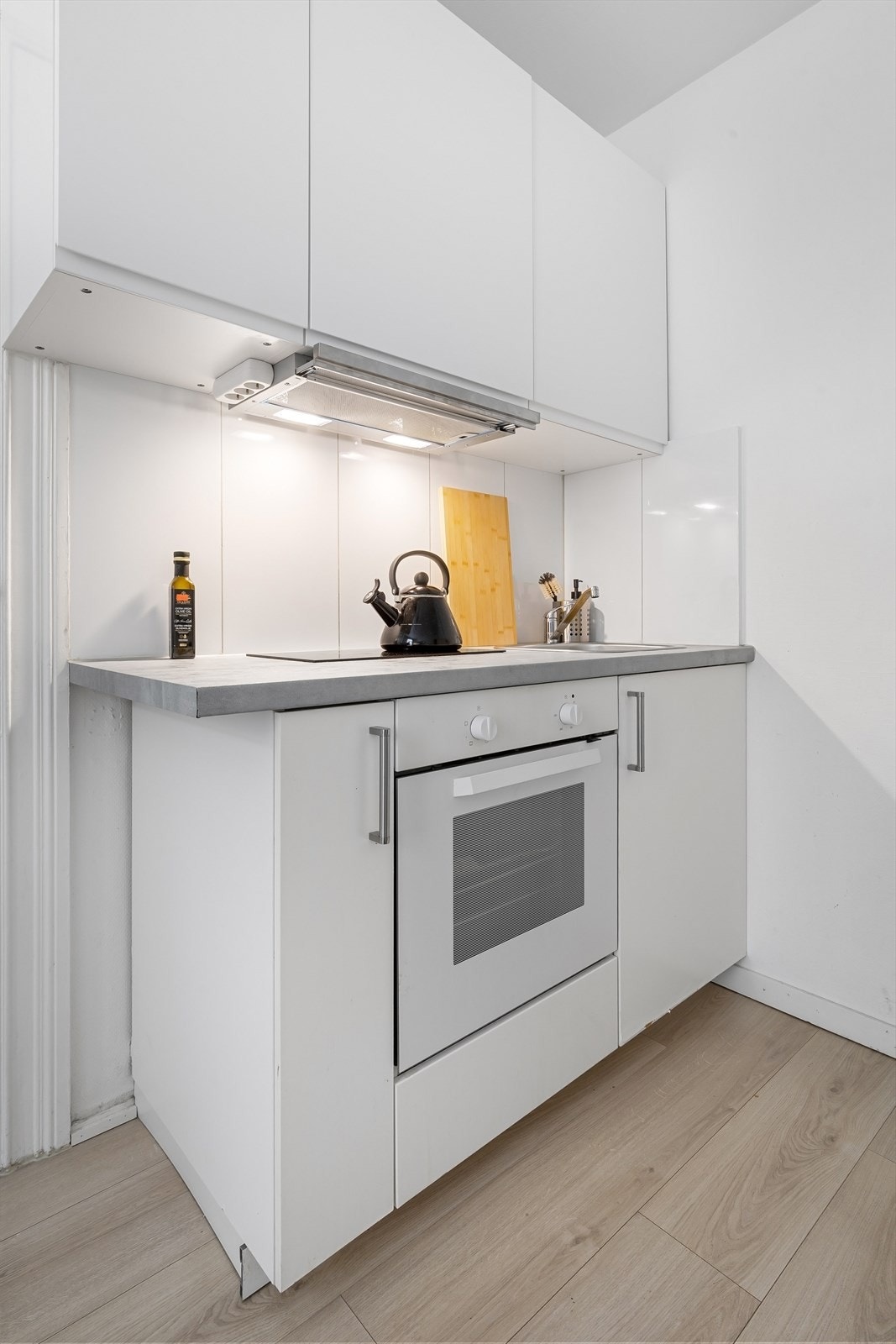 Kjøkken med slette fronter, fliser på vegg, laminat benkeplate og kullfilterventilator. Stekeovn og platetopp er integrert i innredningen. Galleribilde